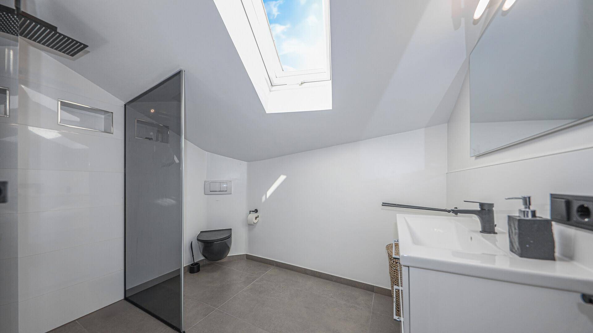 Modernes Badezimmer mit begehbarer Dusche, wandhängendem WC und einem Oberlicht für natürliches Licht.
