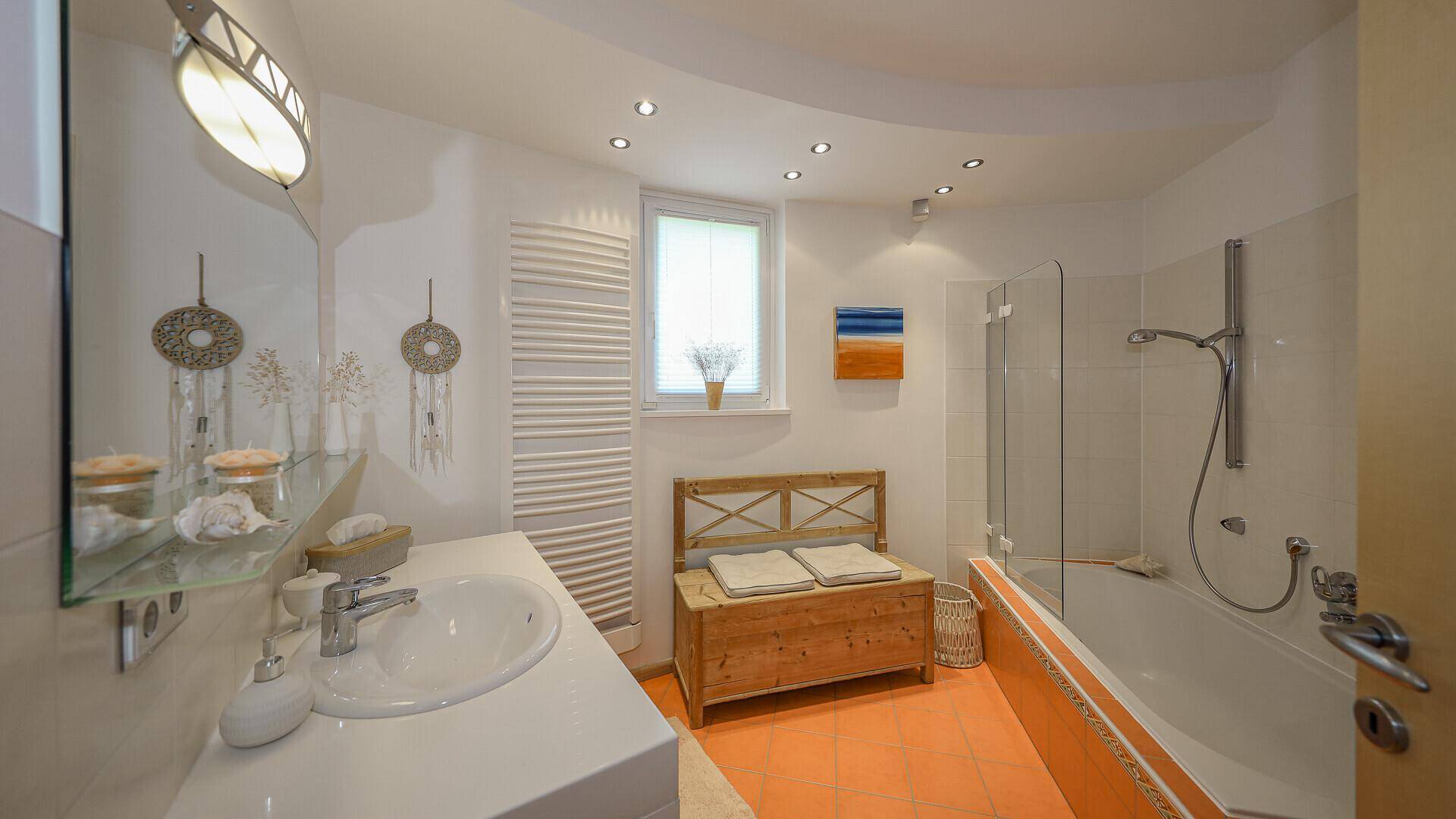 Helles Badezimmer mit Badewanne, Dusche, Einzelwaschbecken und Fenster, ausgestattet mit einem Handtuchheizkörper.