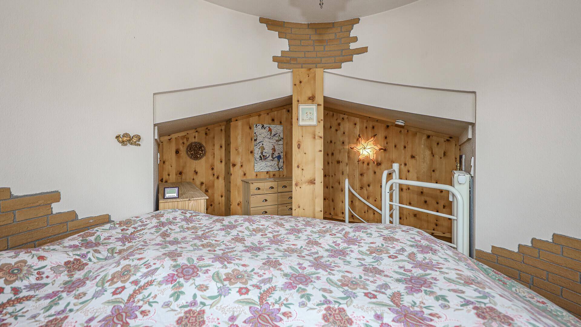 Schlafzimmer mit Doppelbett und Zugang zu einem weiteren Bereich mit Holzvertäfelung.