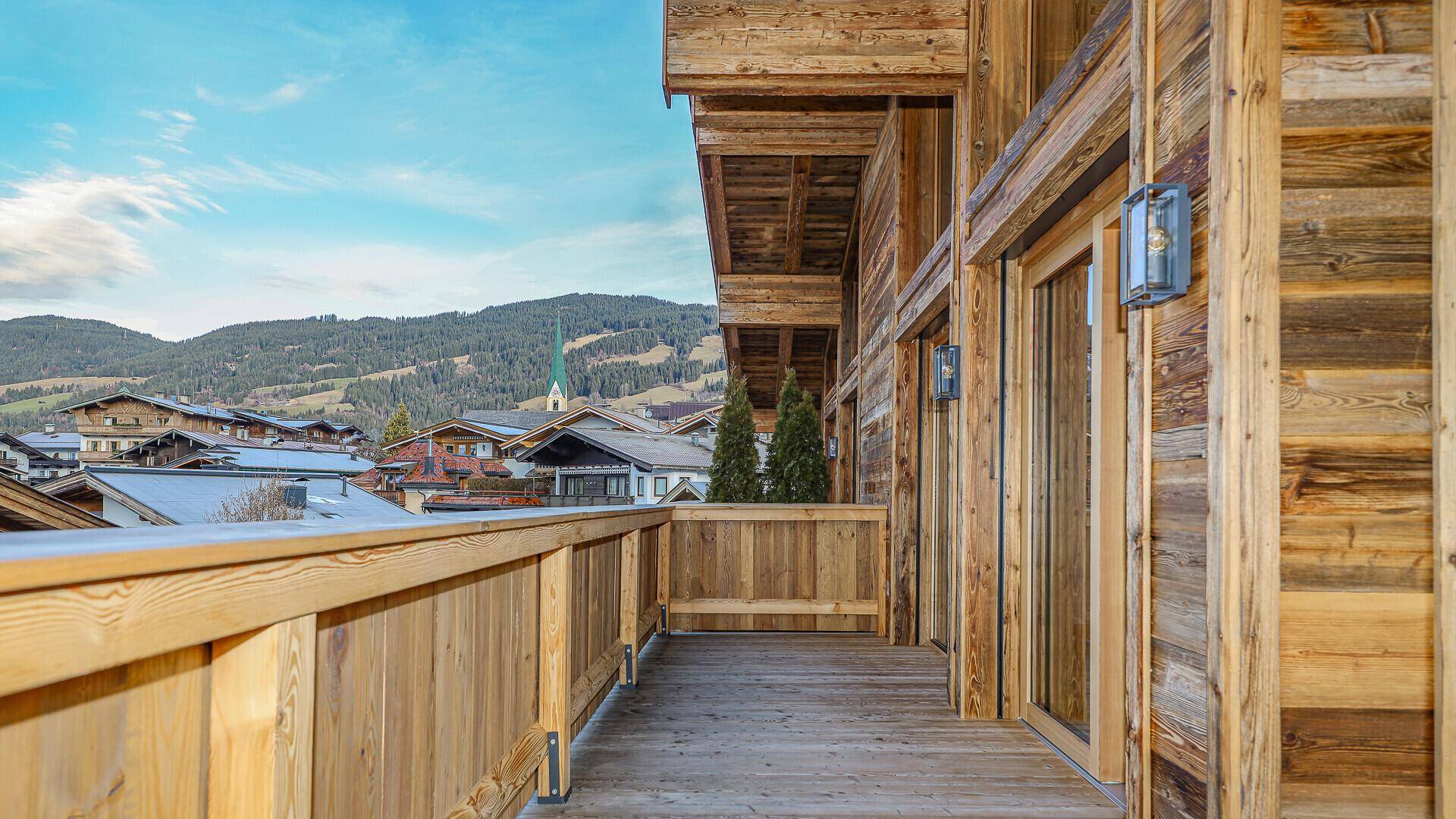 Langer Holzbalkon mit traditionellem Geländer und Blick auf die umliegende Berglandschaft.