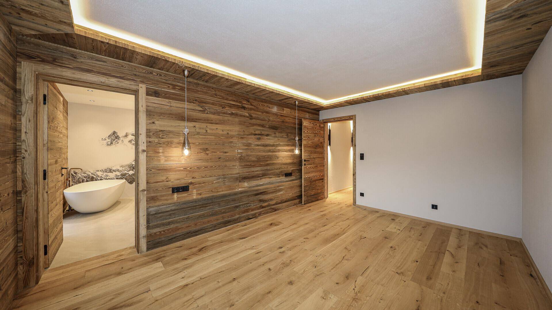 Helles Schlafzimmer mit Holzwänden und Zugang zu einem modernen Badezimmer mit freistehender Wanne.