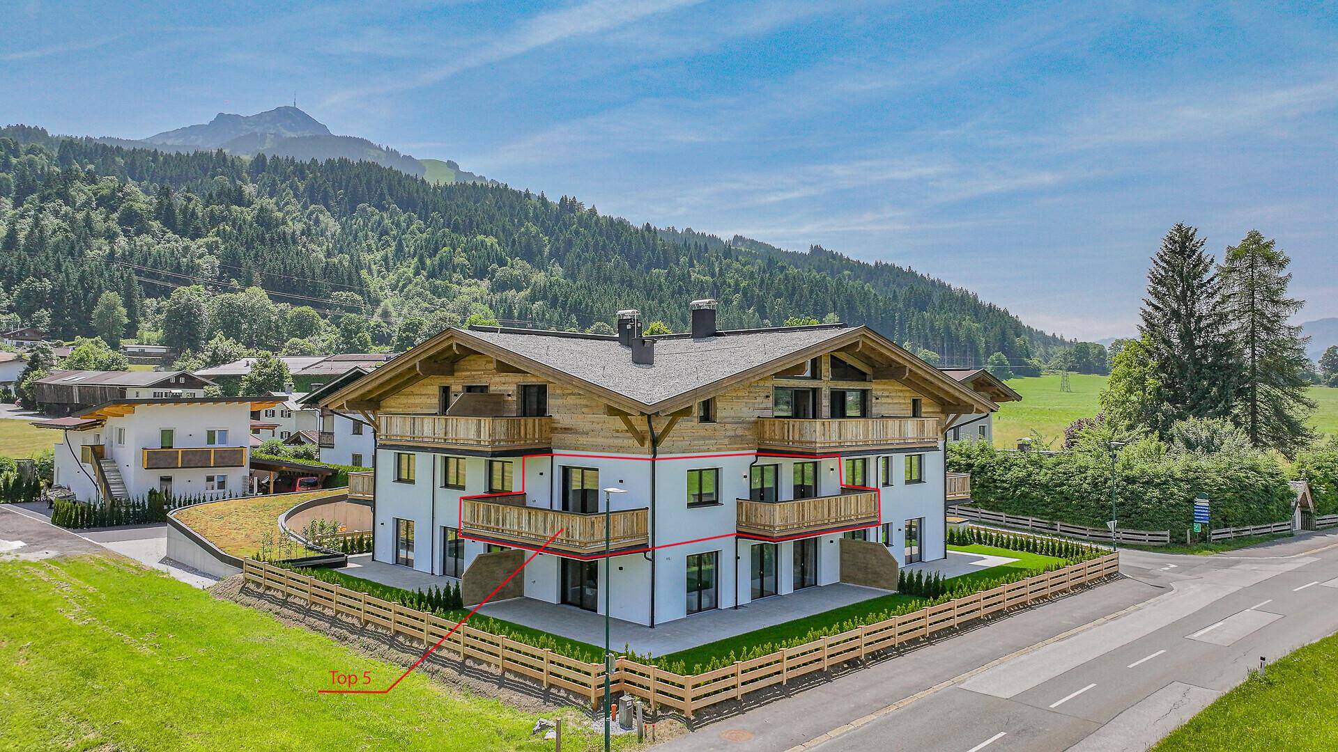 Modernes Mehrfamilienhaus im alpinen Stil mit markierter Wohneinheit und Bergblick.