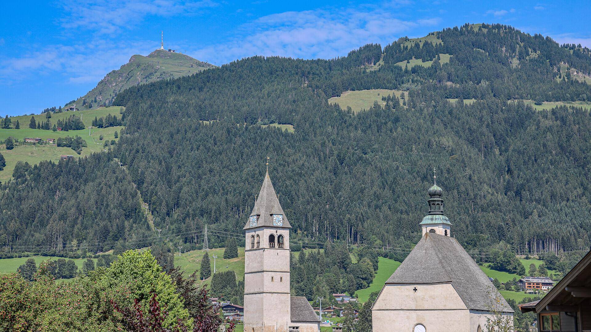 Grüne Berglandschaft mit traditioneller Kirche und bewaldeten Hängen unter blauem Himmel.