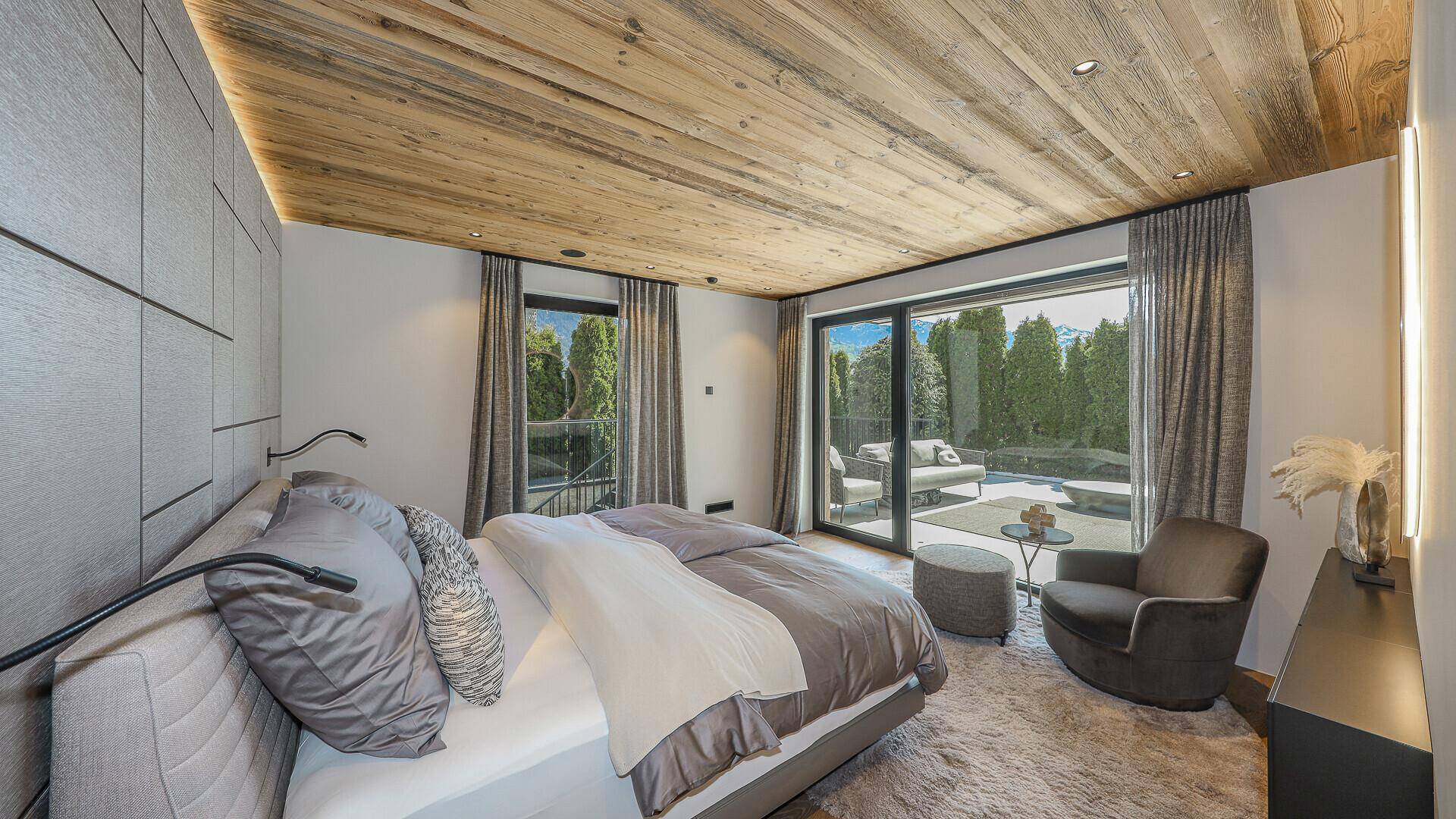 Modernes Schlafzimmer mit Holzbalkendecke, großem Bett und Zugang zu einer Außenterrasse.