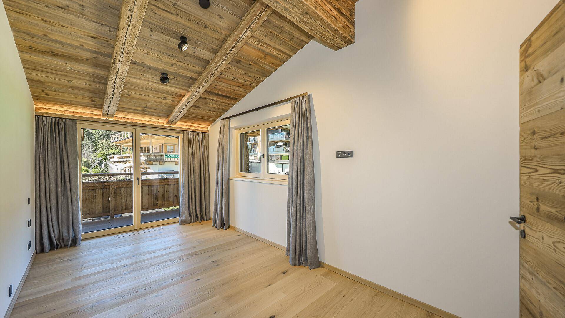 Geräumiges Schlafzimmer mit Holzbalkendecke, Parkettboden und Zugang zu einem Balkon.