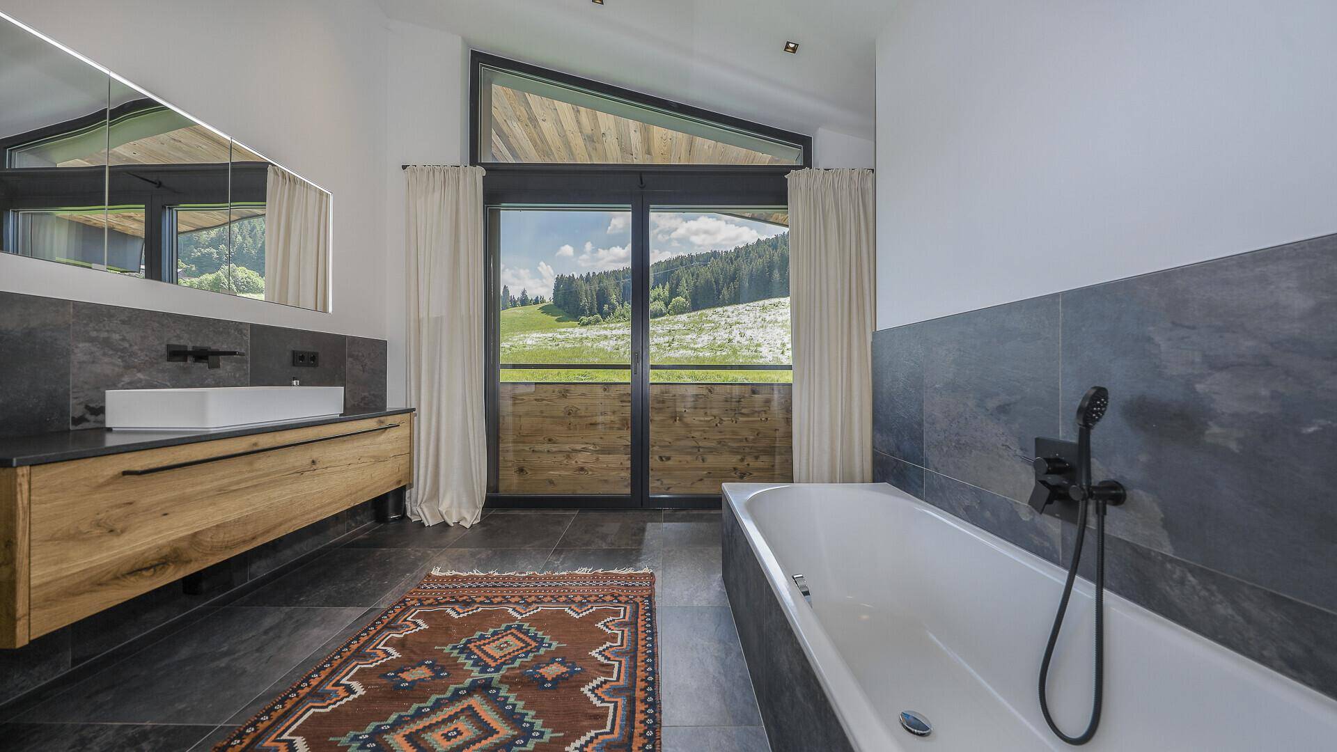 Modernes Badezimmer mit Badewanne, schwebendem Waschtisch und Panoramablick auf die Berge.