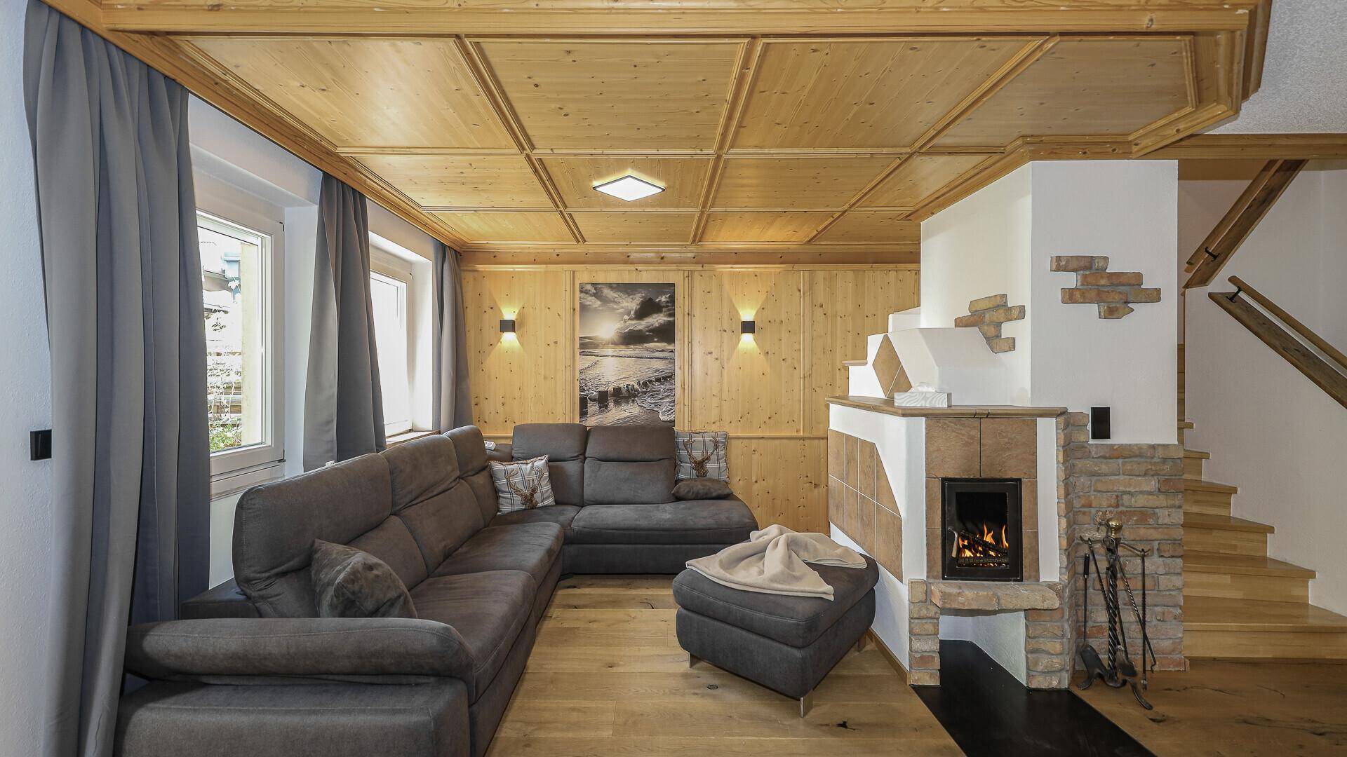 Komfortables Wohnzimmer mit großem Sofa, modernem Kamin und rustikaler Holztäfelung an den Wänden.