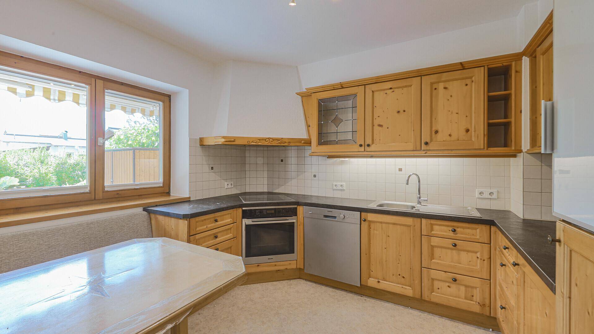Traditionelle Holzküche mit Einbaugeräten, Fliesenrückwand und Fenster mit Blick ins Grüne.