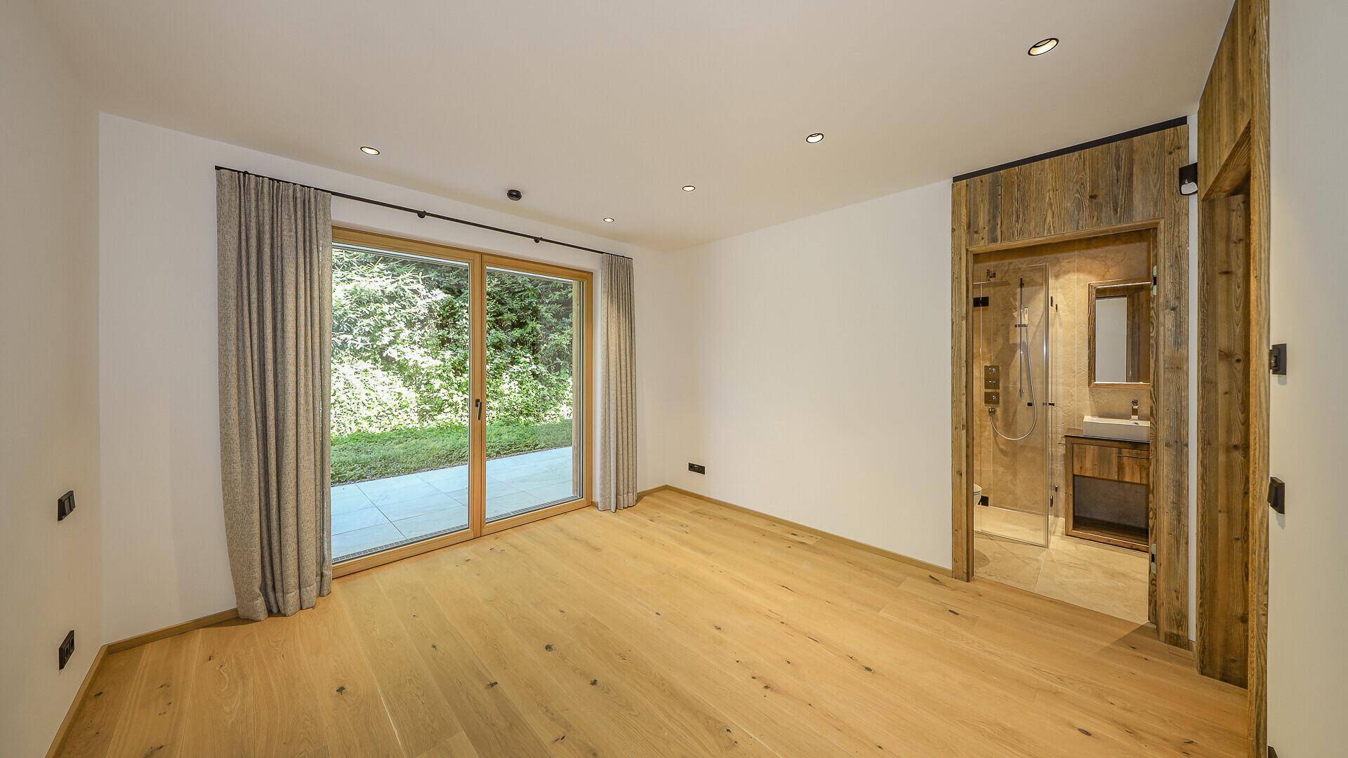 Geräumiges Schlafzimmer mit Holzboden und großen Schiebetüren zum Garten.
