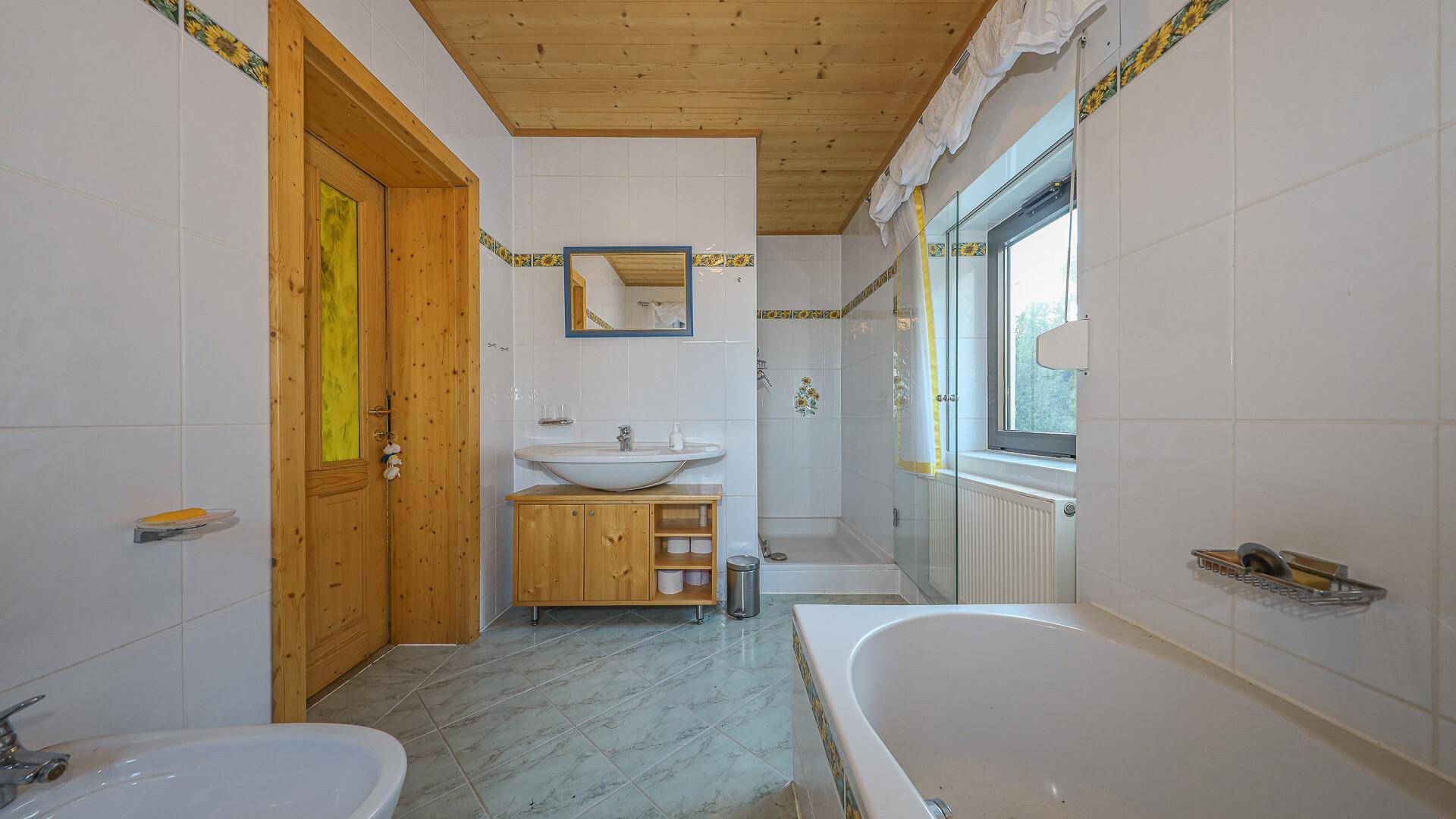 Helles Badezimmer mit Fliesenboden, Badewanne, Dusche und Fenster.