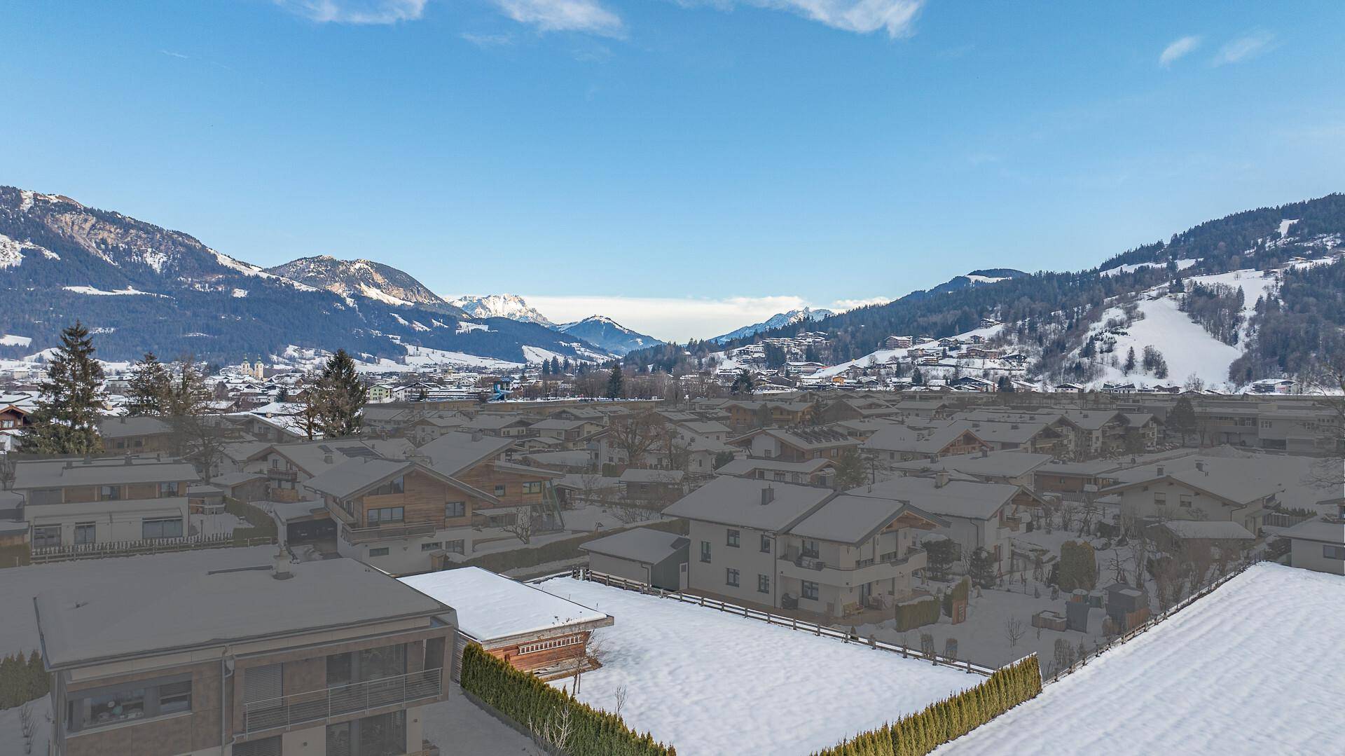 Luftaufnahme einer verschneiten Siedlung in den Bergen mit weitem Blick auf die umliegende Landschaft.