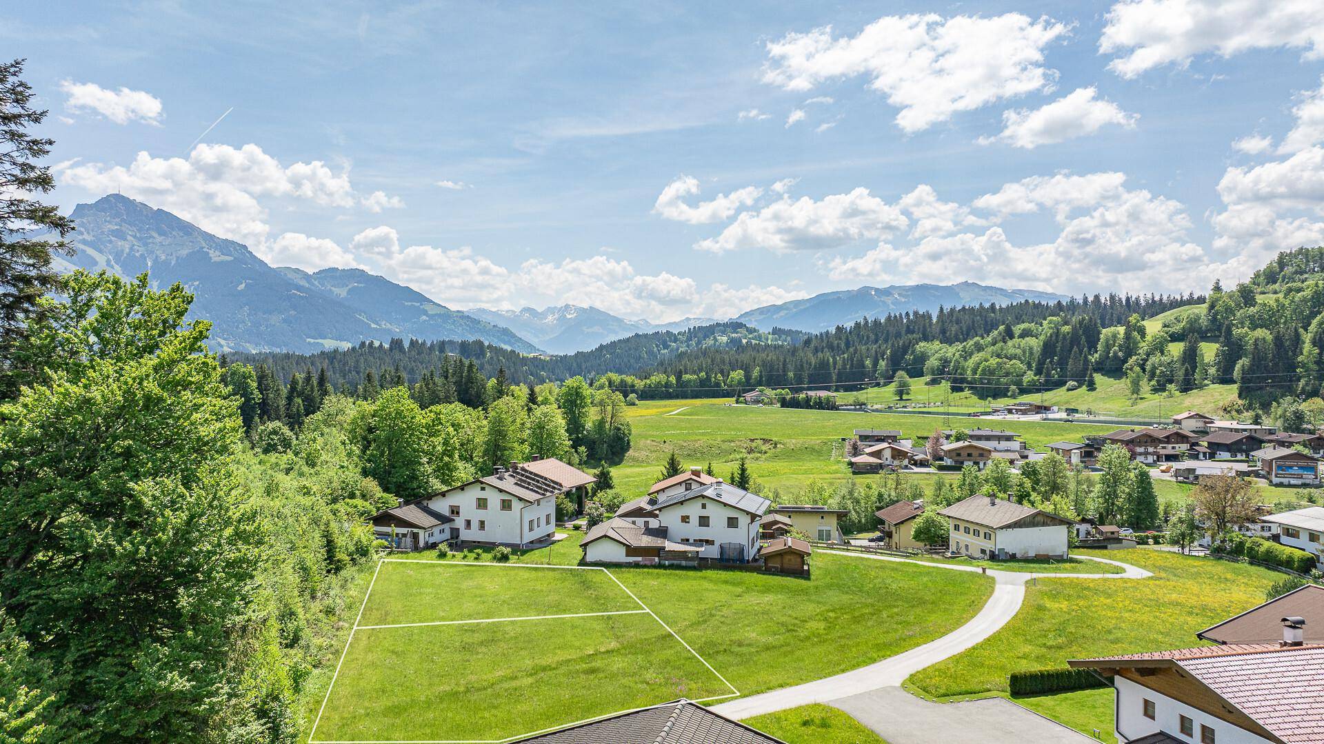 Weitläufige grüne Landschaft mit Häusern und einem freien Grundstück unter einem weiten Himmel.