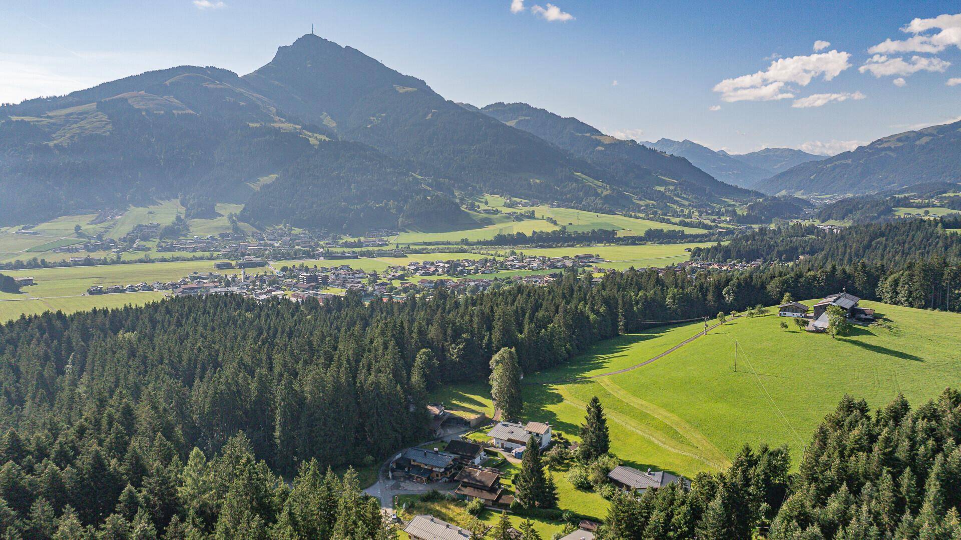 Weitläufige Landschaftsaufnahme eines Tals mit einer Ortschaft, Wäldern und Bergen im Hintergrund.