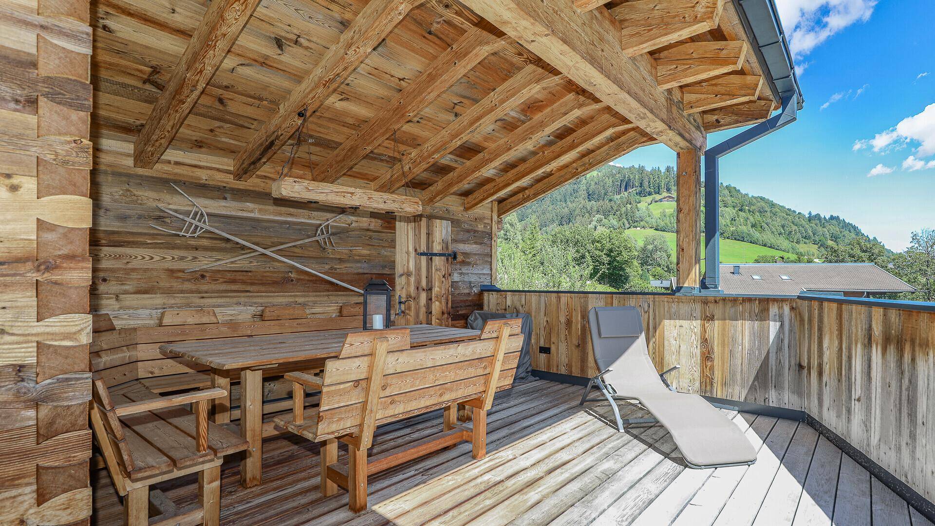 Überdachter Holzbalkon mit rustikalen Möbeln und Blick auf die grüne Landschaft.