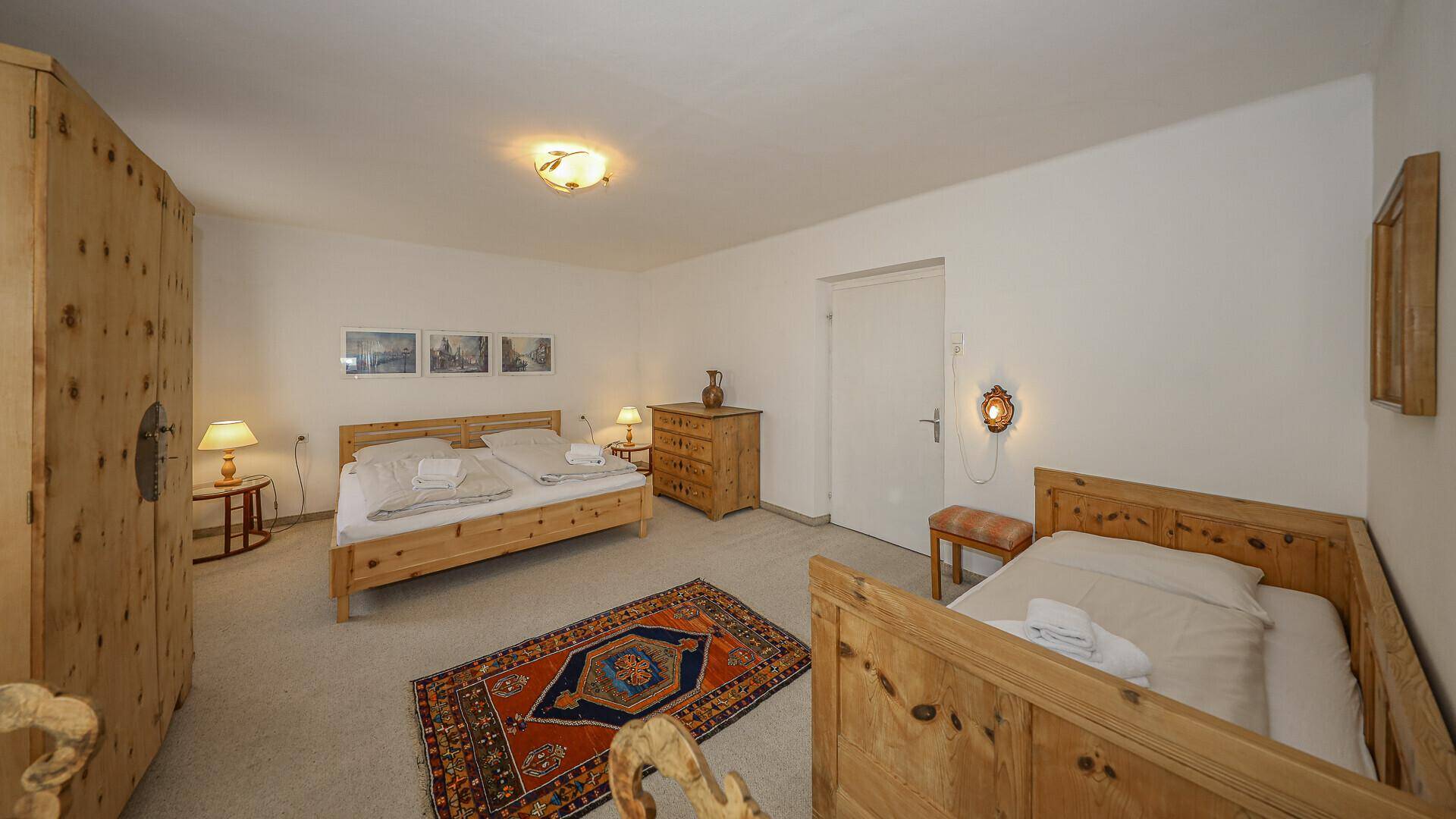 Helles Schlafzimmer mit zwei Einzelbetten, Holzmöbeln und einem Teppich im traditionellen Stil.