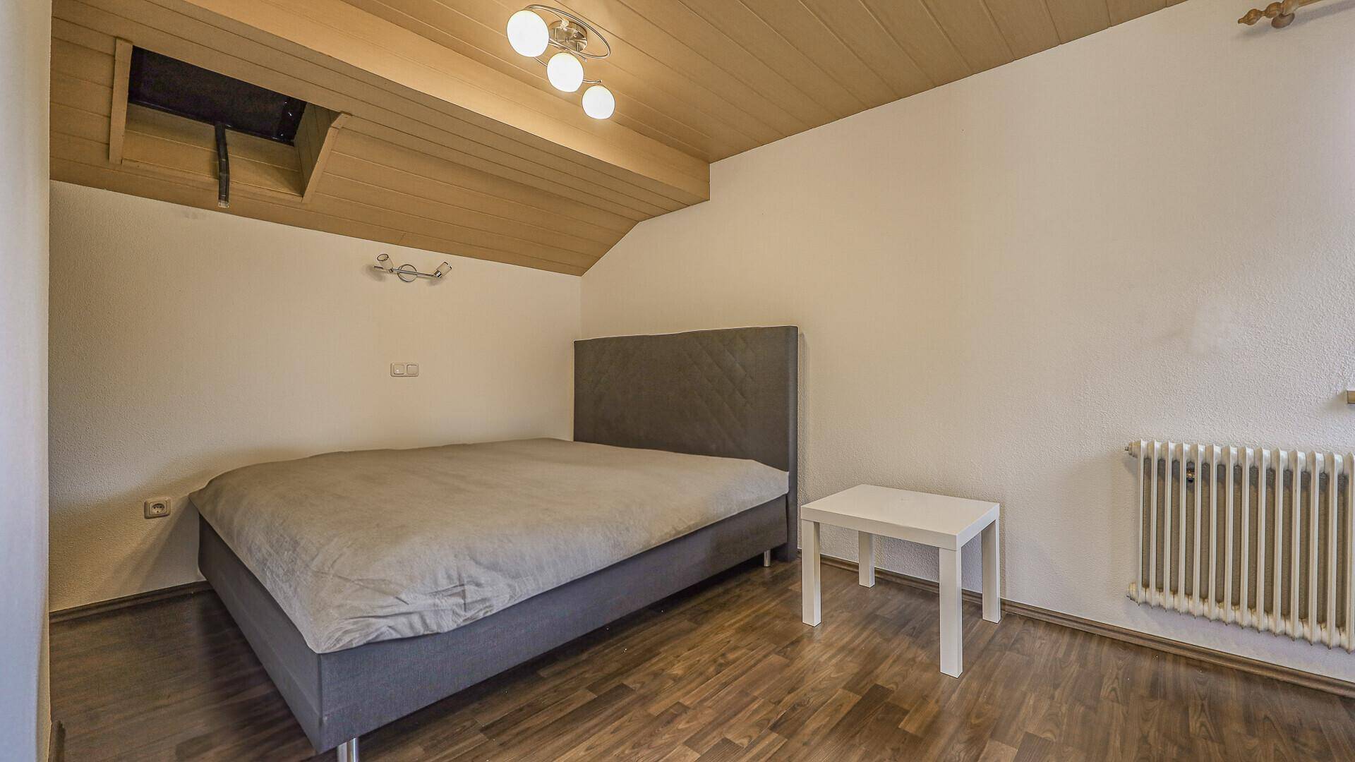 Helles Schlafzimmer mit Holzwandverkleidung und Dachschräge, ausgestattet mit einem Bett.