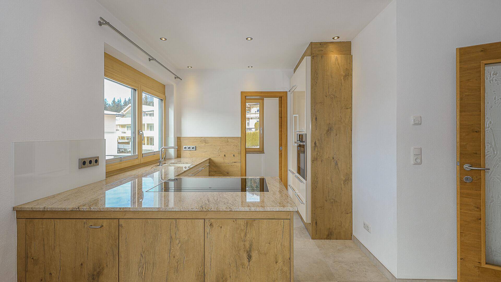 Moderne Küche mit Holzelementen, Granitarbeitsplatte und integriertem Kochfeld.