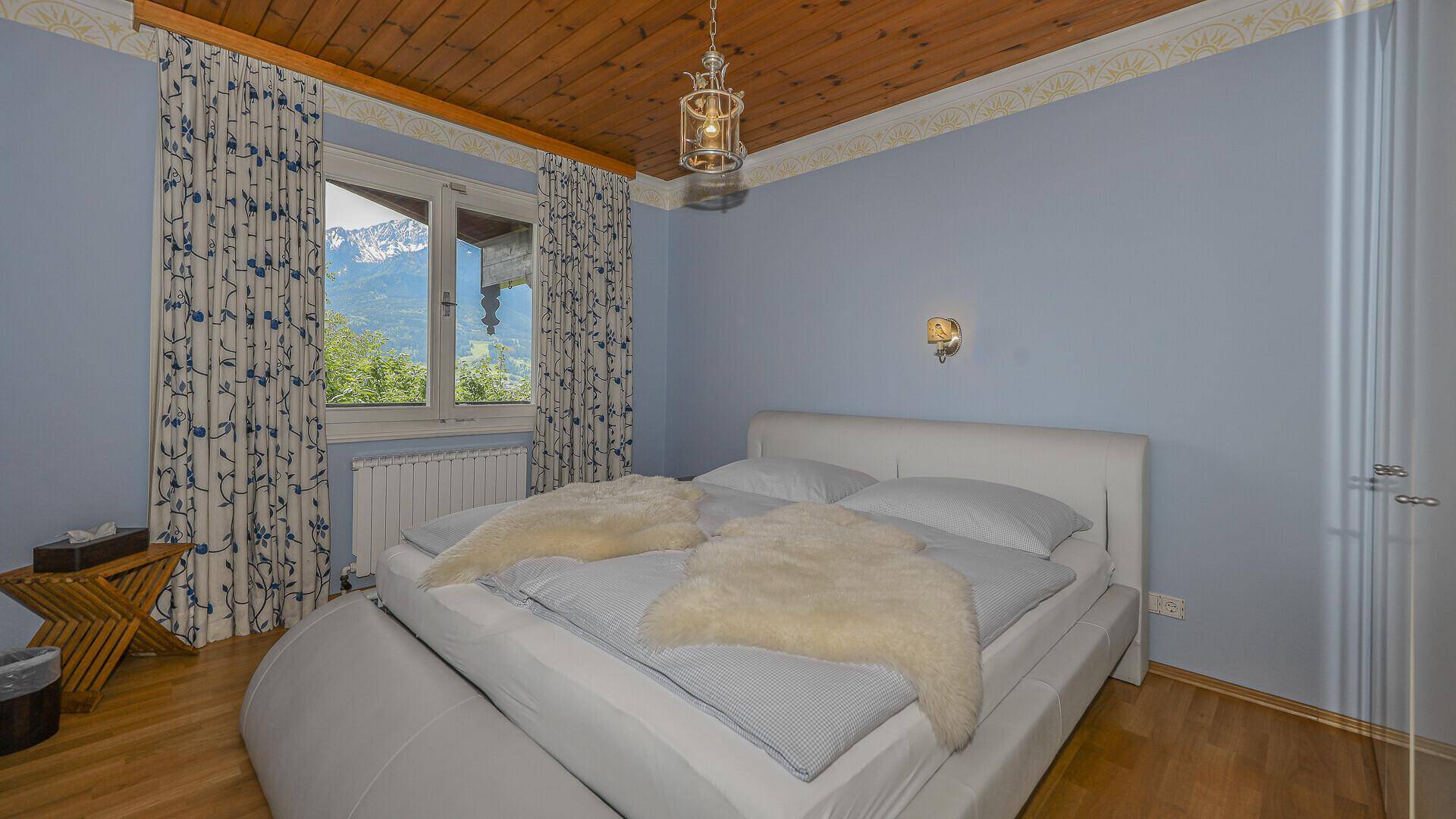 Schlafzimmer mit Doppelbett, blauen Wänden, Parkettboden und Bergblick durch das Fenster.