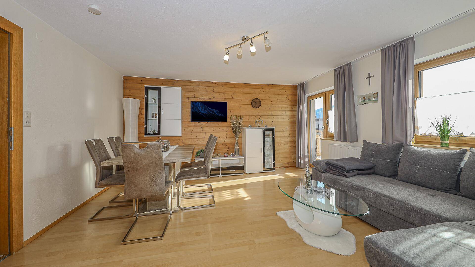 Moderner Wohn-Essbereich mit Holzwand, großem Sofa und Esstisch, hell und einladend.