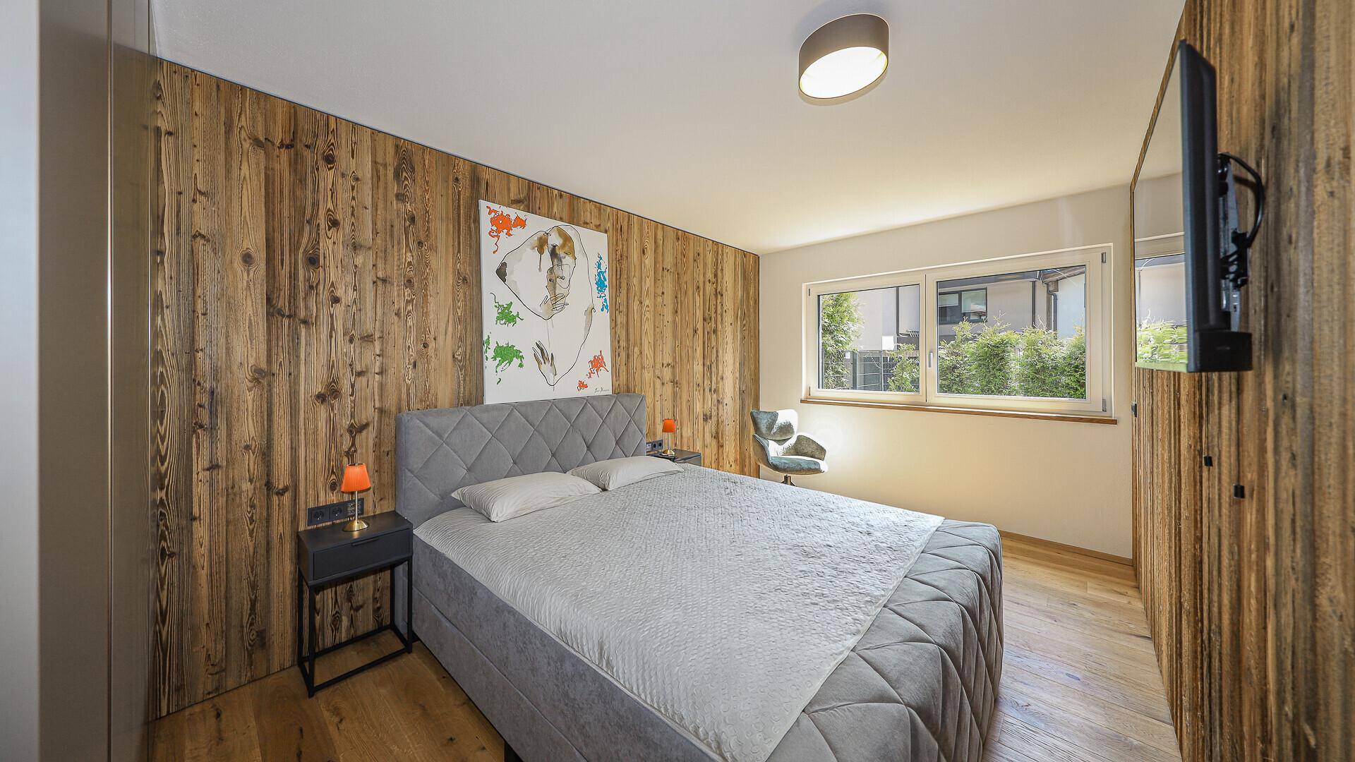 Helles Schlafzimmer mit Holzwand, Doppelbett und Blick ins Grüne.