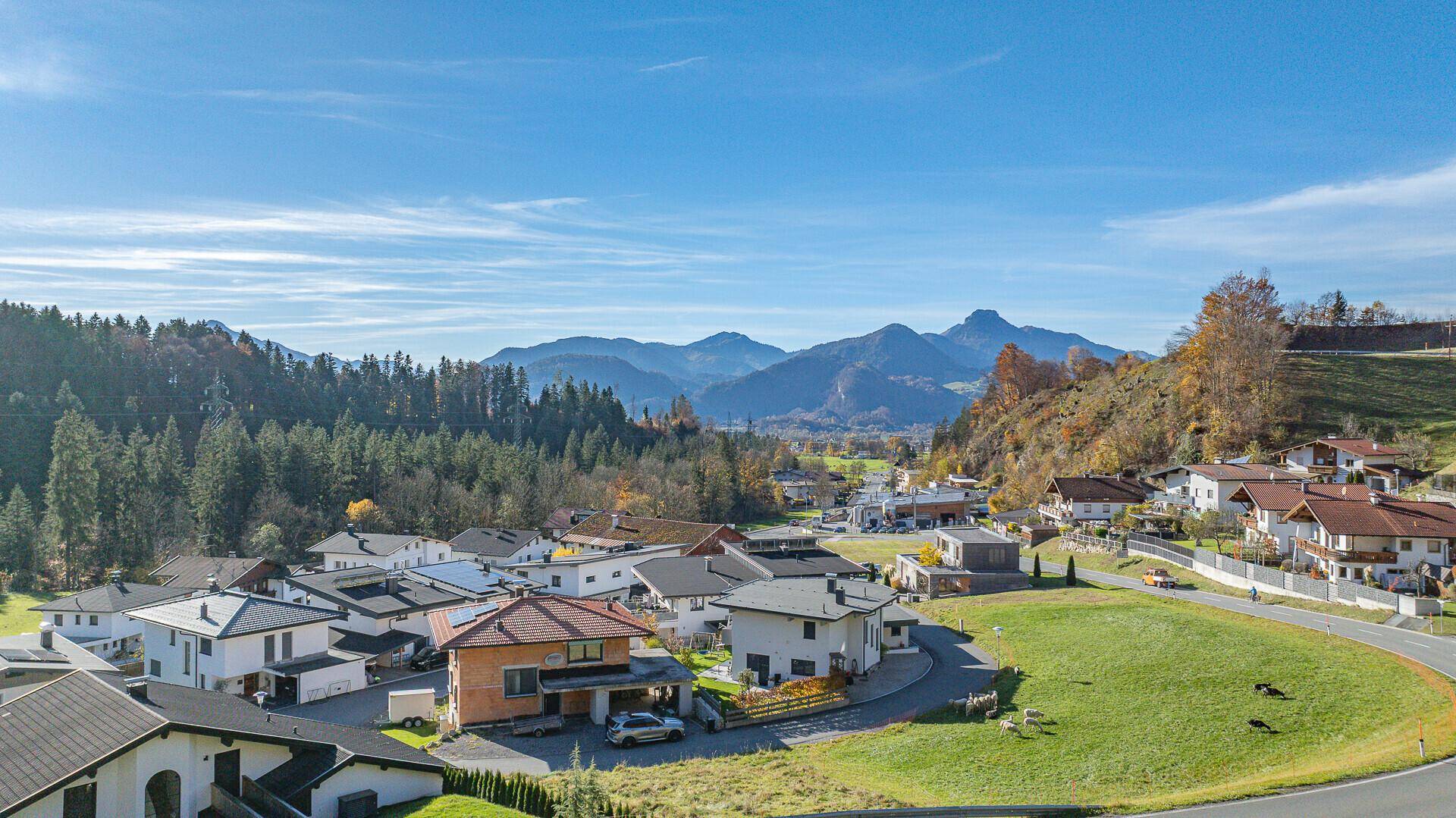 Weitläufiger Blick über eine Siedlung in einem Tal mit bewaldeten Bergen im Hintergrund.