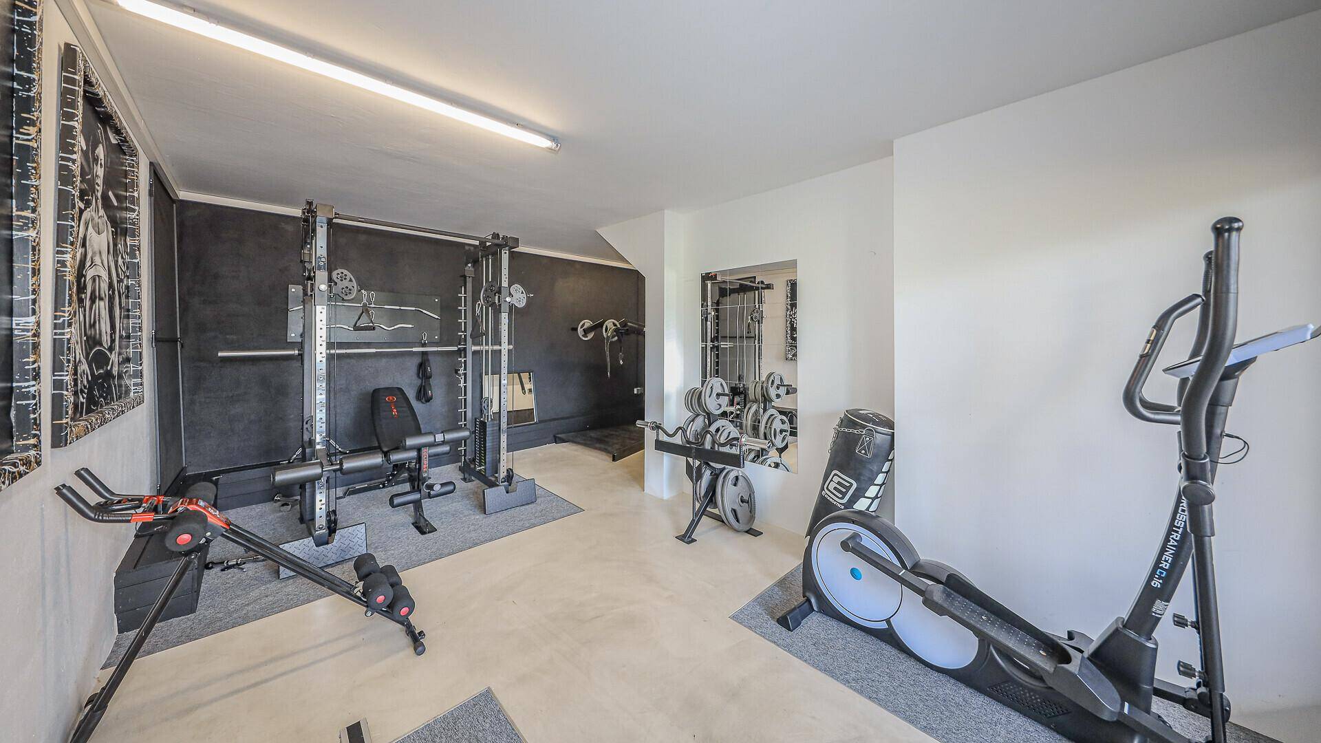 Gut ausgestatteter Fitnessraum mit verschiedenen Trainingsgeräten und Hanteln.