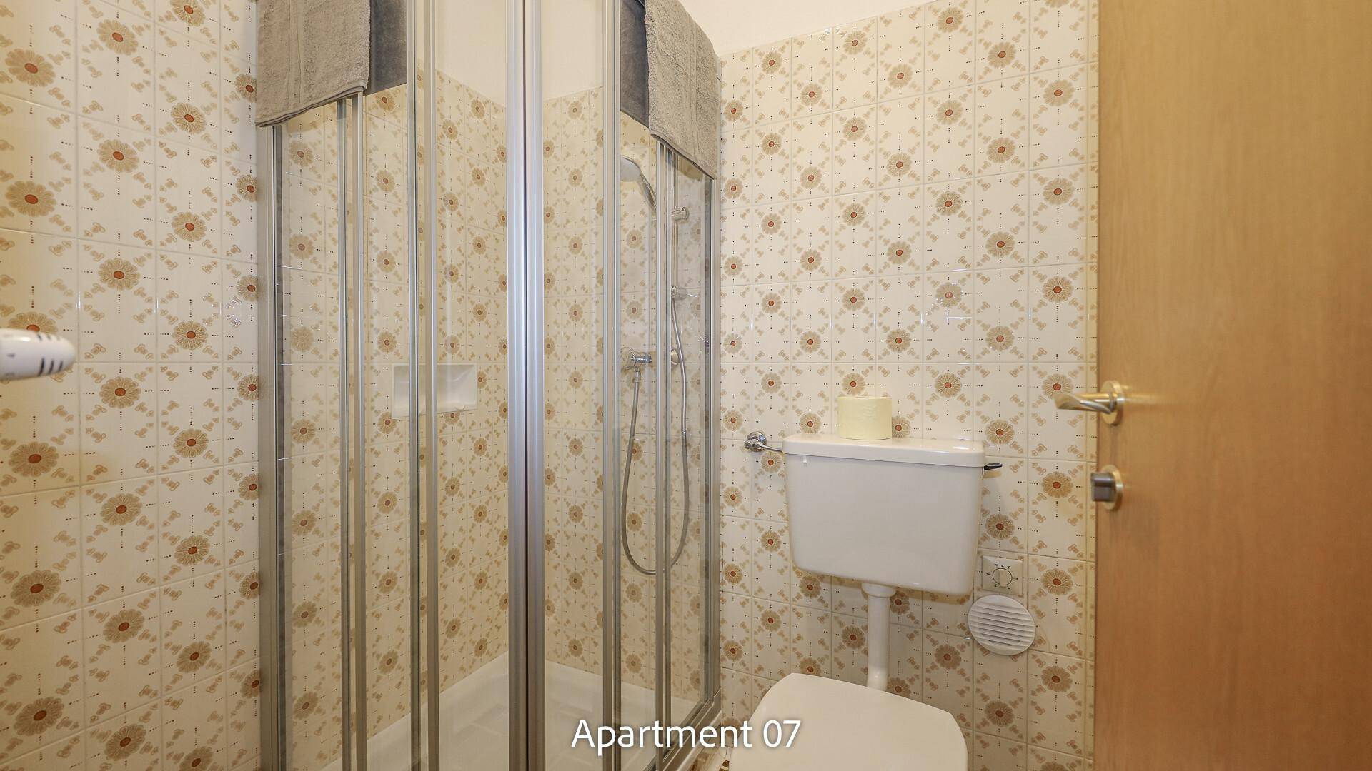 Badezimmer von Apartment 07 mit gemusterten Fliesen, WC und einer Duschkabine.