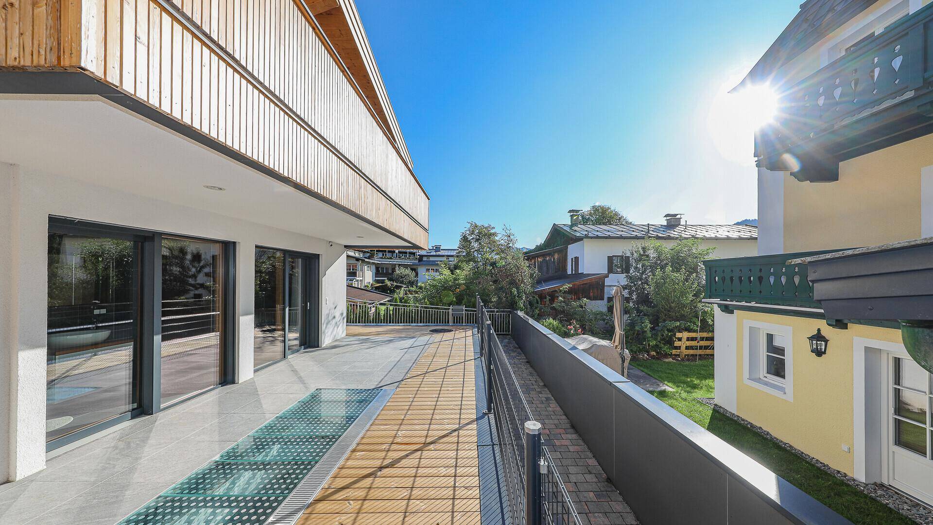 Große Terrasse mit Holzboden, Glasdetails und sonnigem Ausblick auf die Umgebung.