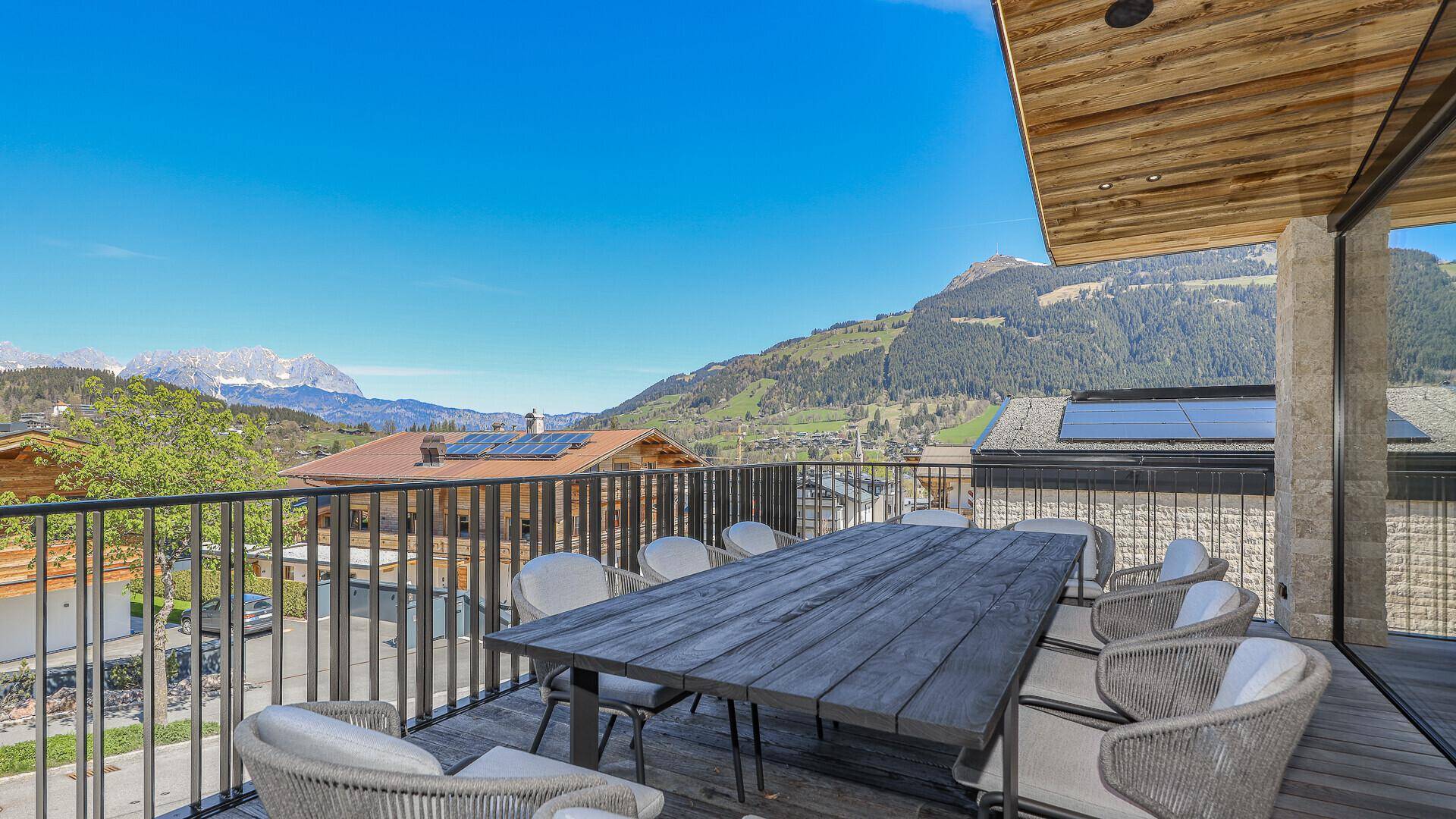 Große Essterrasse mit Holztisch und Stühlen, umgeben von einer malerischen Bergkulisse.