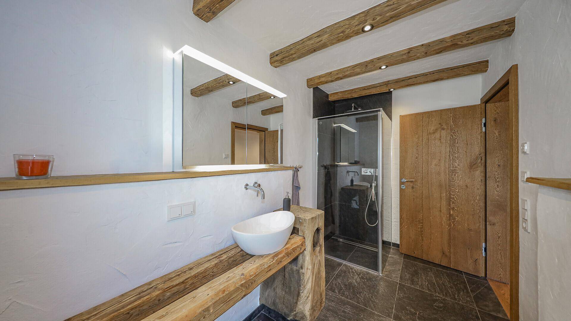 Modernes Badezimmer mit Holzbalken, Natursteinfliesen, Einzelwaschbecken und begehbarer Dusche.