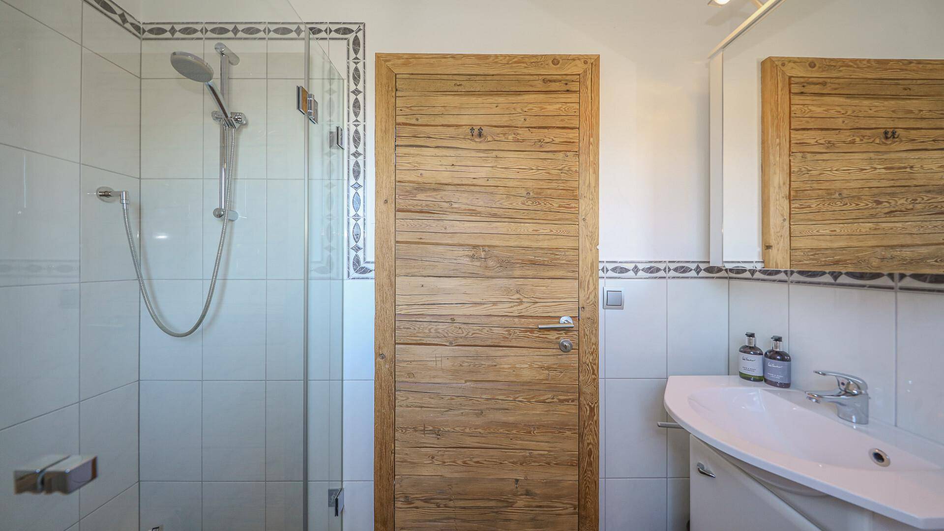Helles Badezimmer mit Duschkabine, Waschbecken und weißen Fliesen.