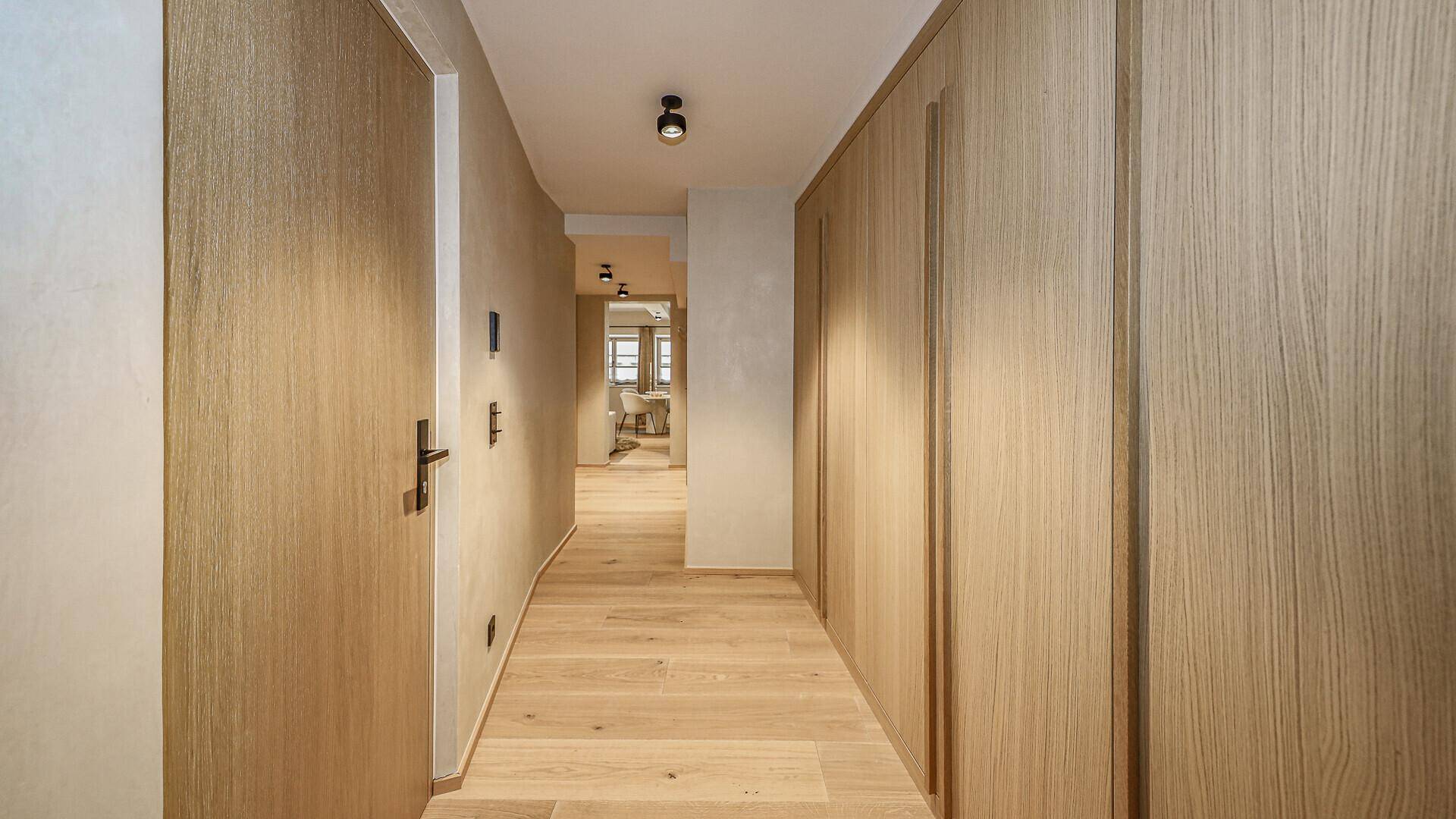Heller Flur mit Holzboden und integrierten Holzschränken, führt zu weiteren Räumen.