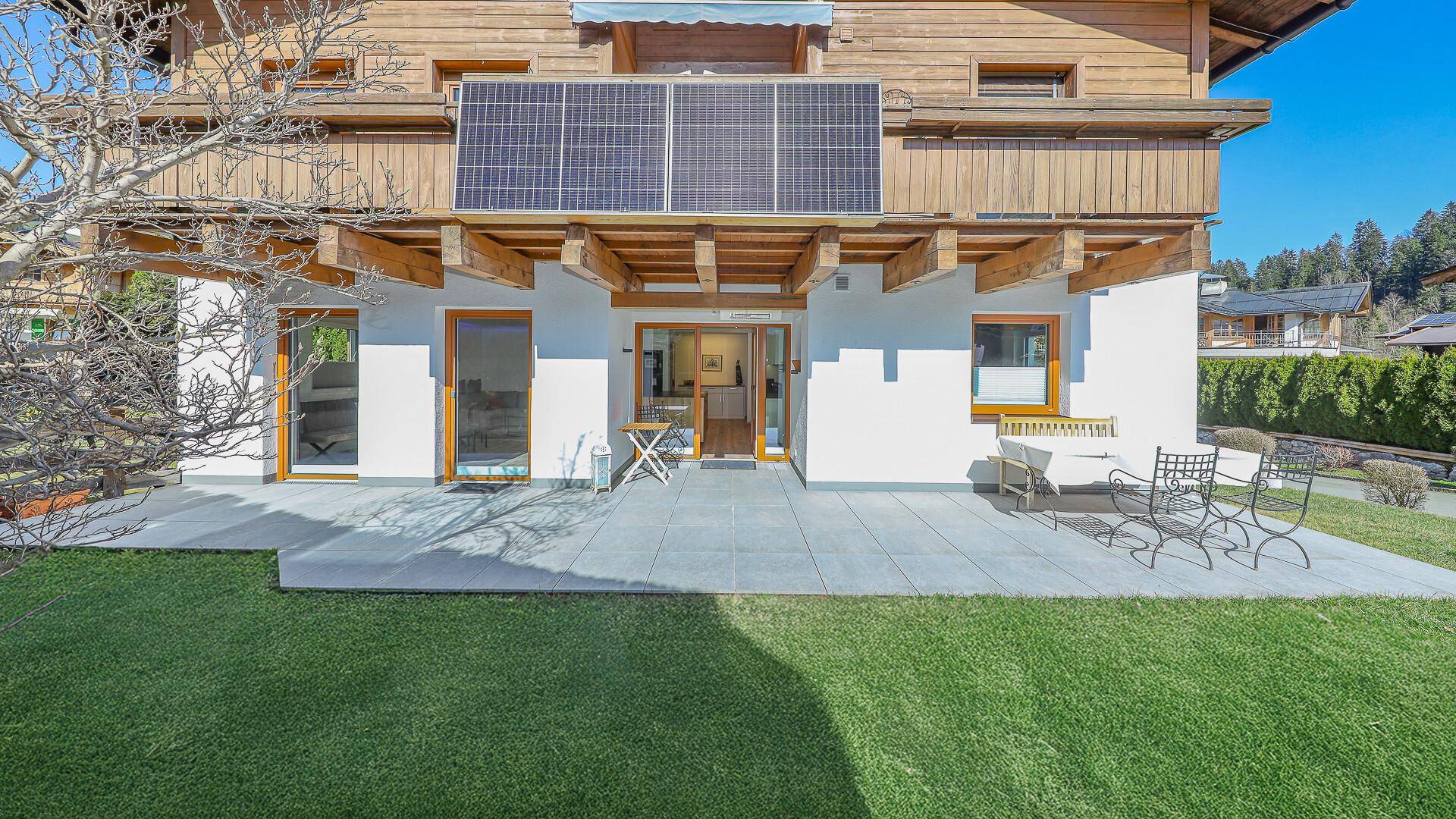 Große Terrasse mit Gartenmöbeln und Rasenfläche vor dem Haus mit Holzbalkonen.