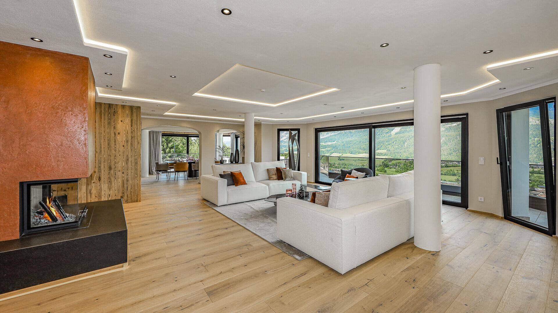 Geräumiges Wohnzimmer mit modernem Kamin, Holzboden und großen Fenstern mit Bergblick.