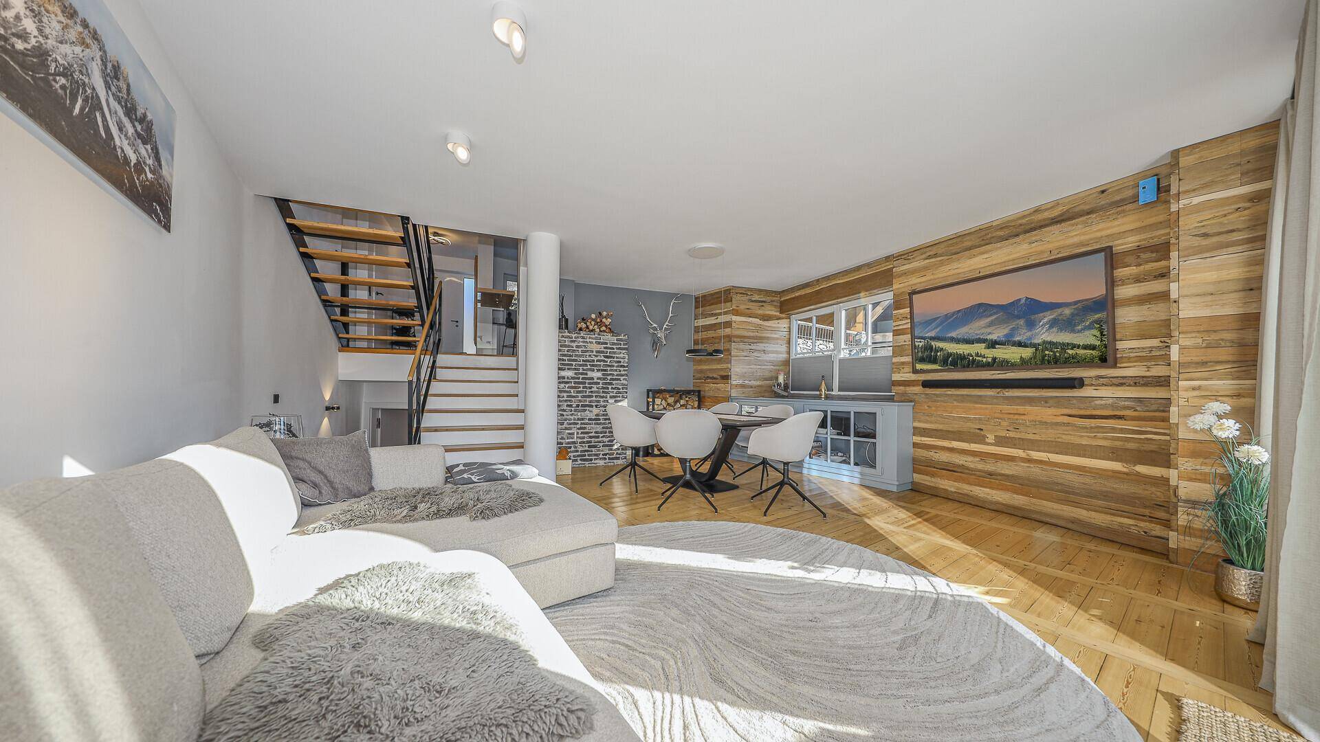 Geräumiger Wohnbereich mit gemütlichem Sofa, Holzwand und offener Treppe, die die verschiedenen Ebenen verbindet.