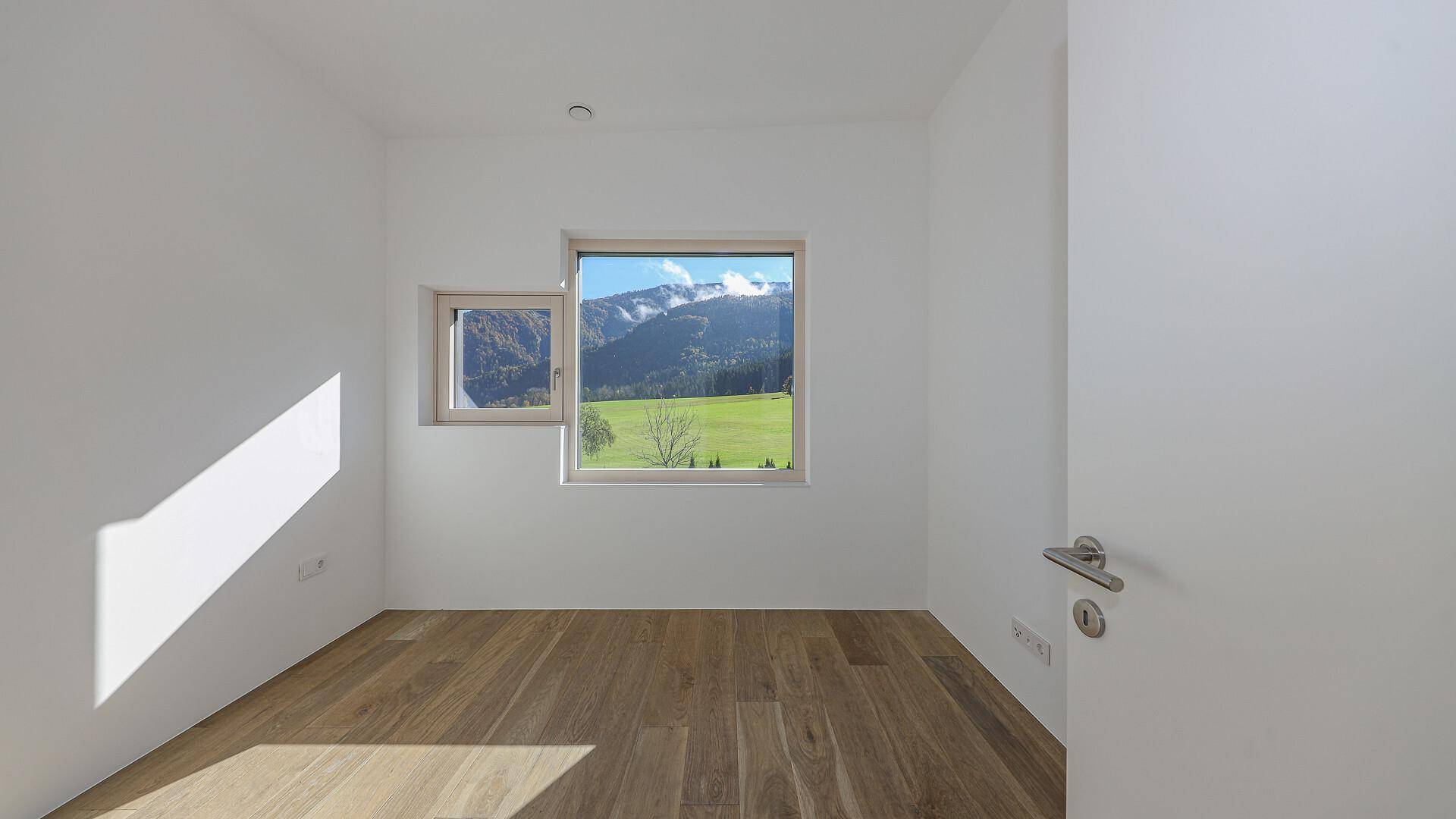 Helles Schlafzimmer mit Holzboden und Fenstern, die einen schönen Blick auf die Berge bieten.