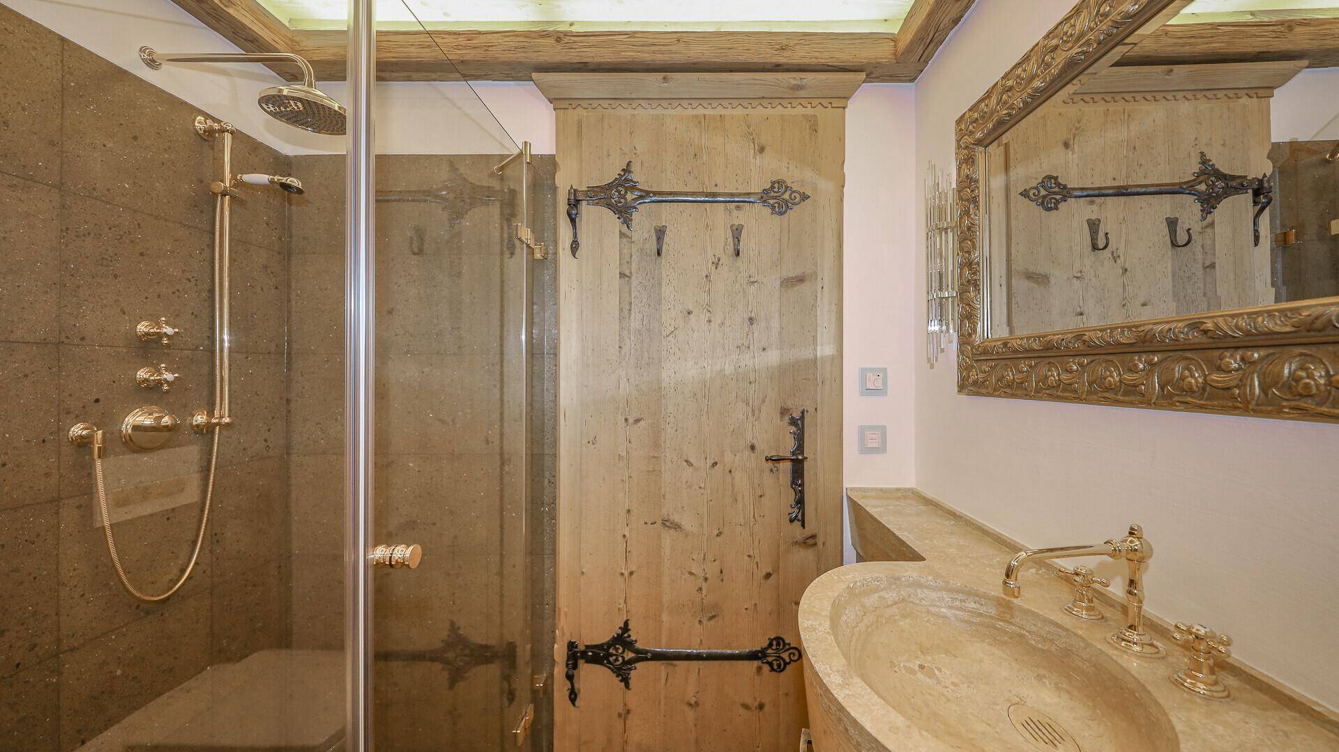 Modernes Badezimmer mit begehbarer Dusche, Steinwaschbecken und goldenen Armaturen.