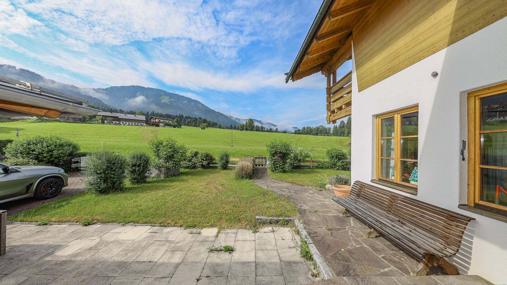 Sonnenterrasse mit Holzbank und Blick auf den Garten und die umliegende Berglandschaft.