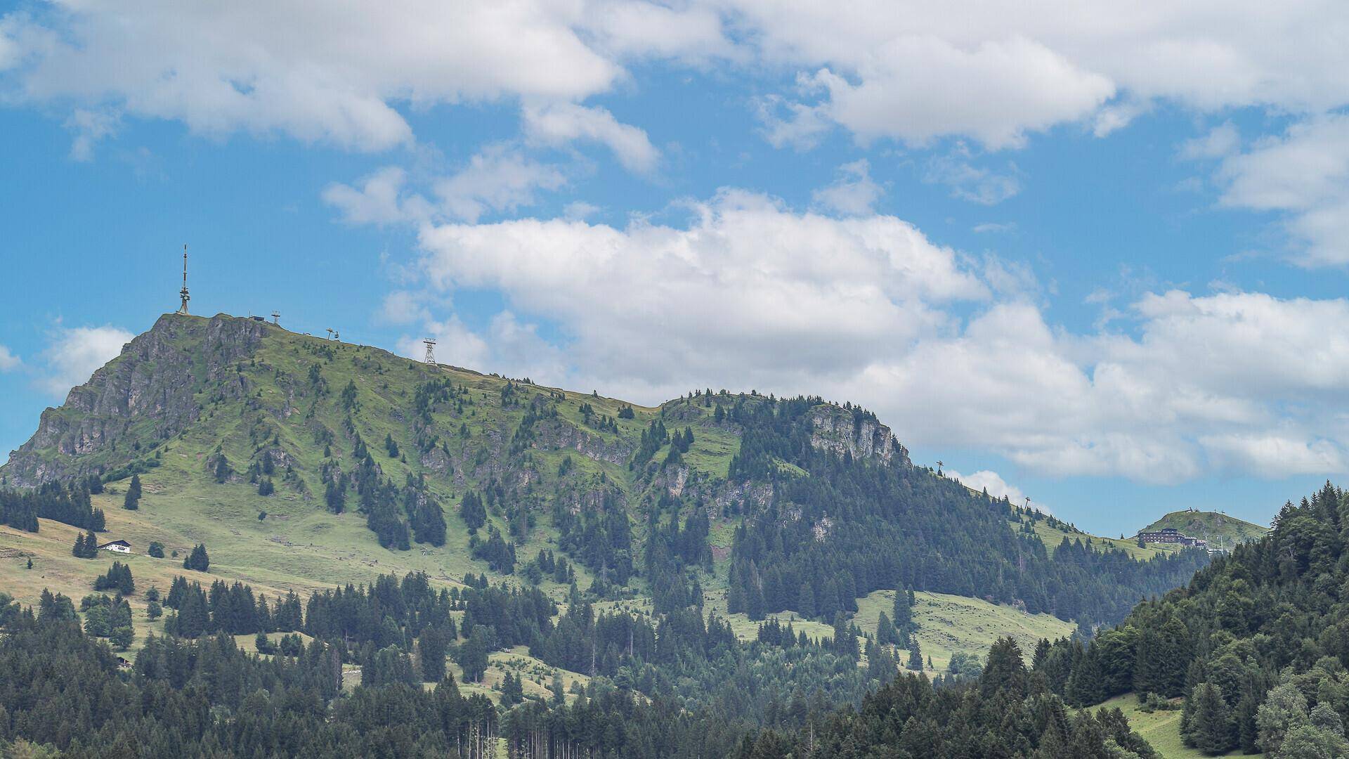 Panoramablick auf einen markanten grünen Berg mit Sendeturm und bewaldeten Hängen.