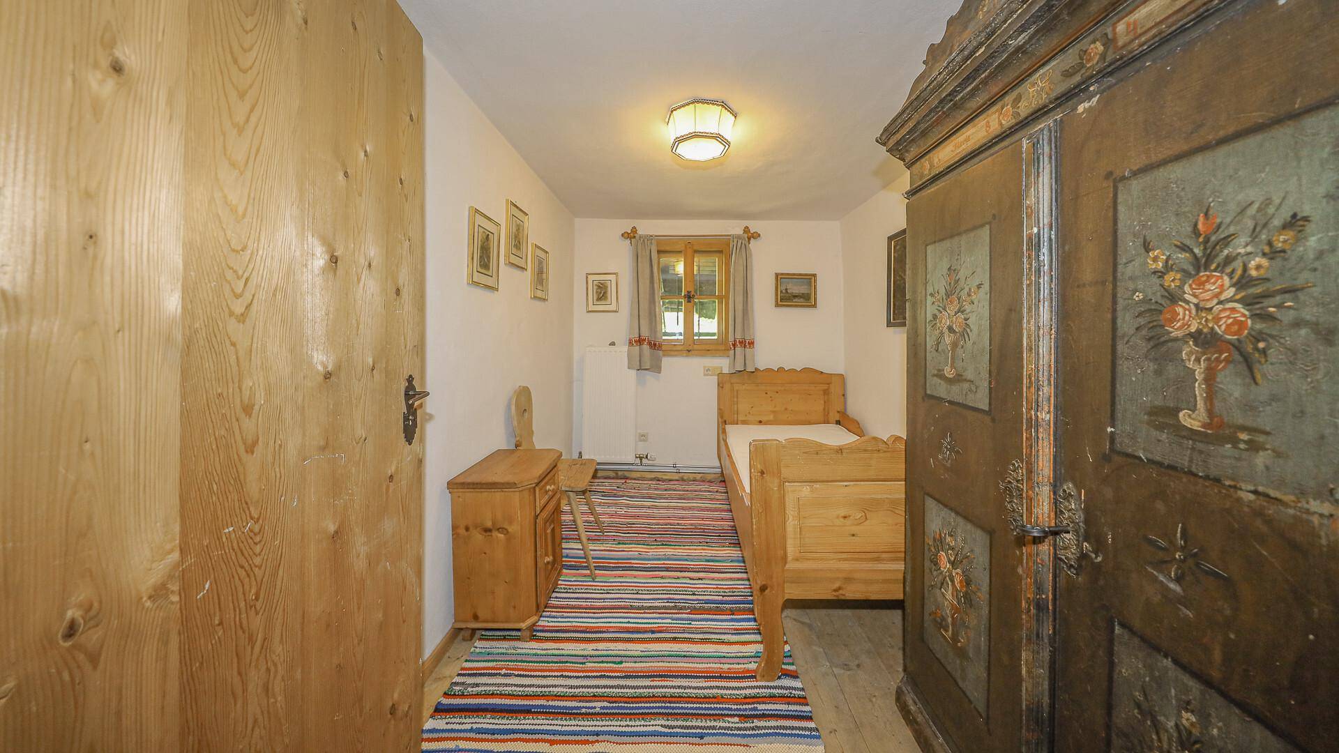 Kleines Schlafzimmer mit Einzelbett, Holzboden und traditionellem Teppich.