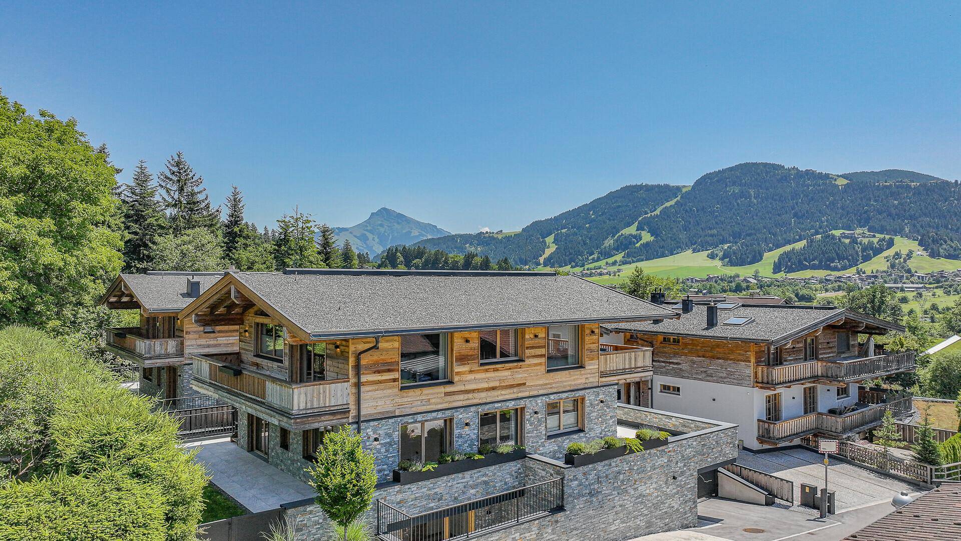 Luxuriöses Chalet mit Holzbalkonen und Steinfassade, eingebettet in eine grüne Berglandschaft.