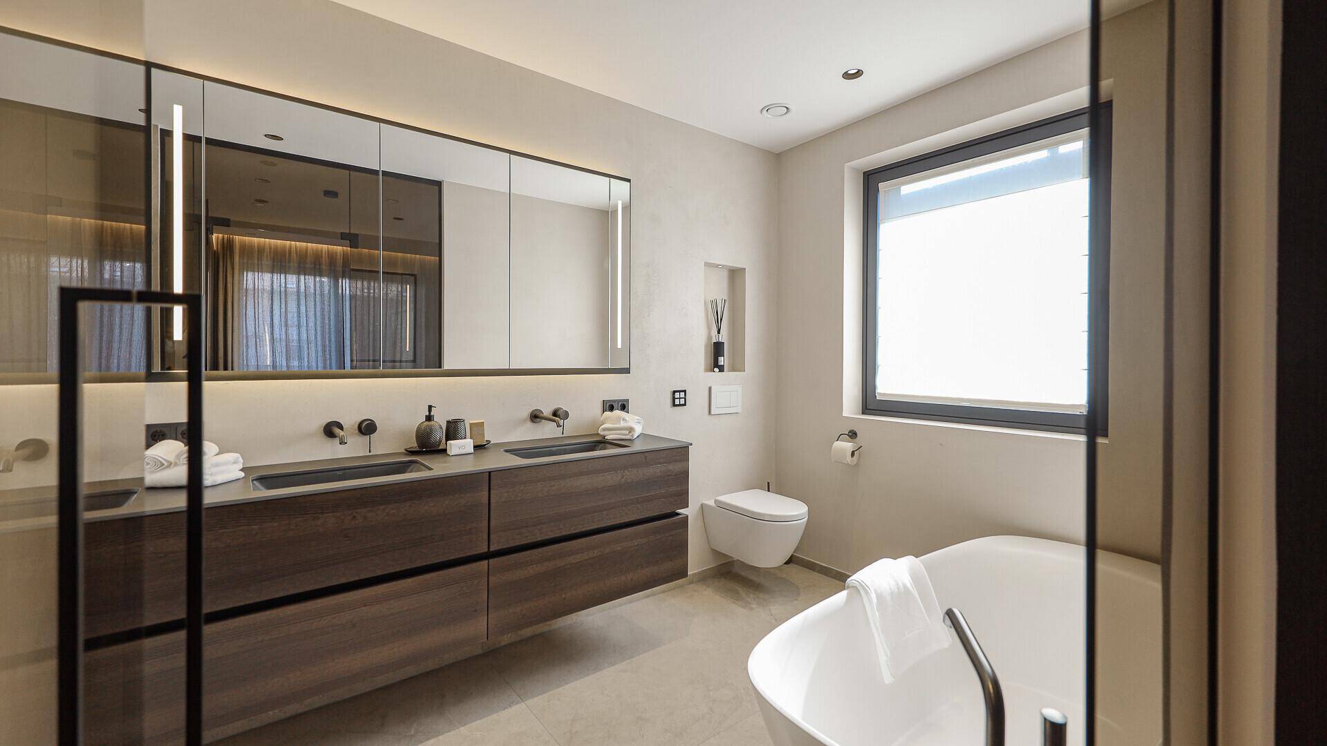 Luxuriöses Badezimmer mit Doppelwaschbecken, freistehender Badewanne und großer Spiegelfront.