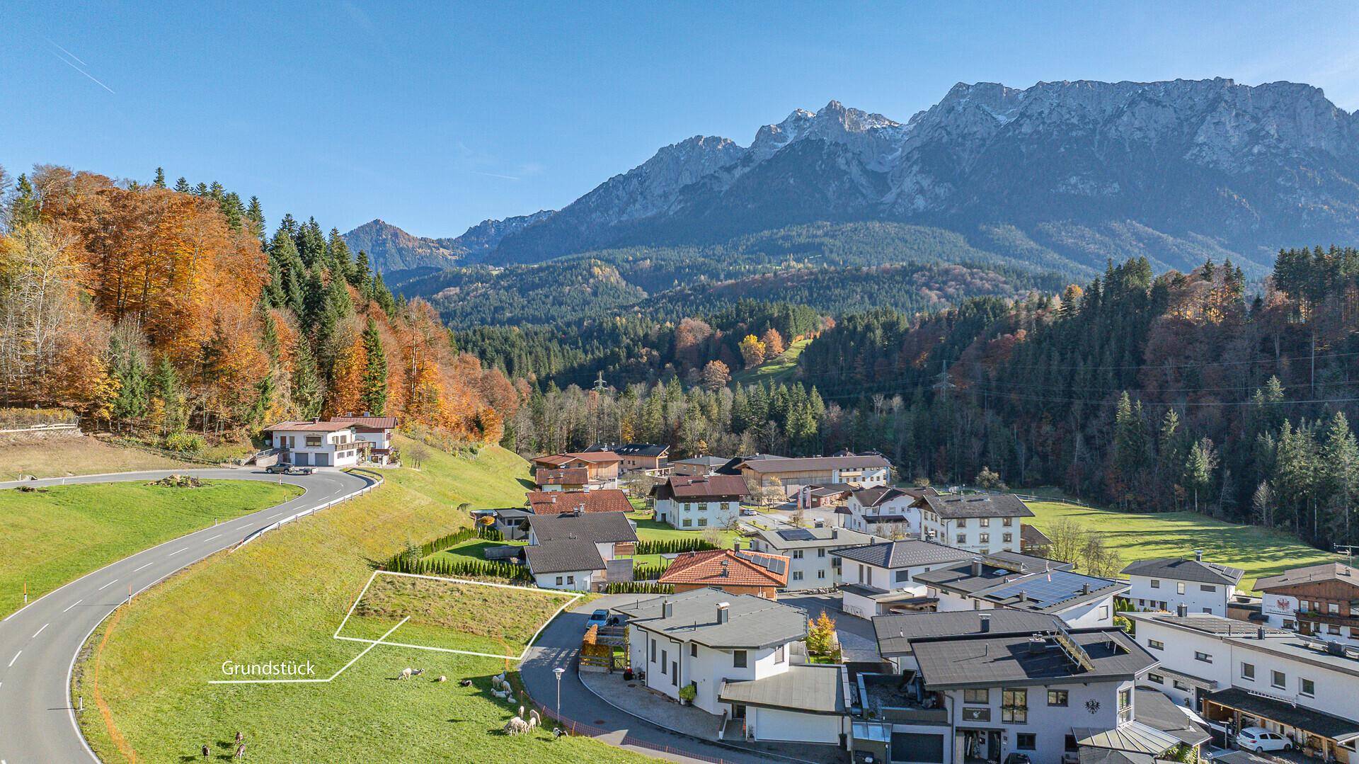 Luftaufnahme eines Grundstücks in einer ländlichen Siedlung mit beeindruckendem Bergpanorama.
