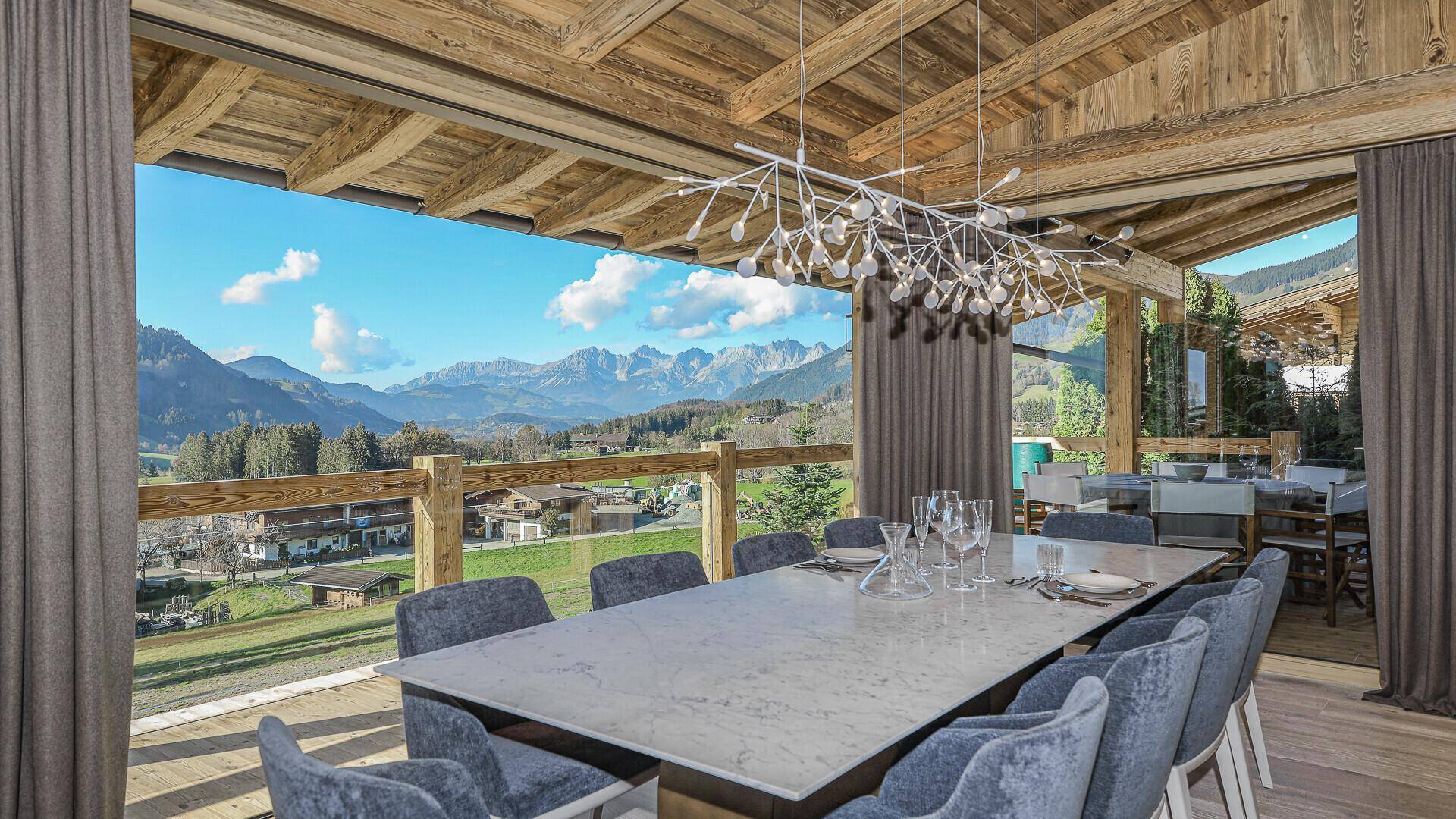 Heller Essbereich mit großem Tisch, moderner Beleuchtung und beeindruckendem Bergblick.