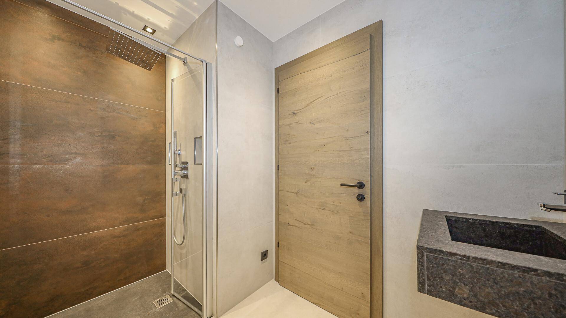 Modernes Badezimmer mit begehbarer Dusche, dunklem Waschtisch und Holztür.