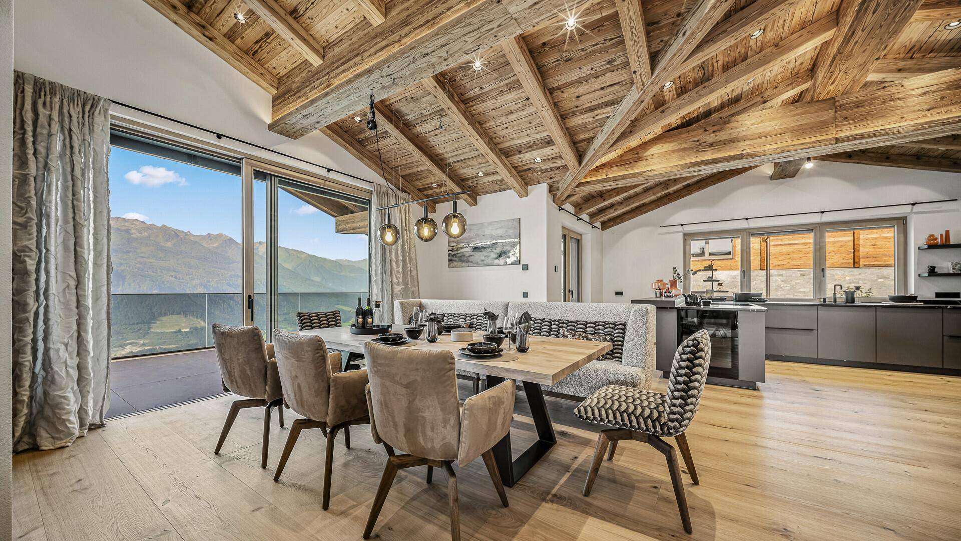 Eleganter Essbereich mit Holzbalkendecke, großem Esstisch und offener Küche im Hintergrund.