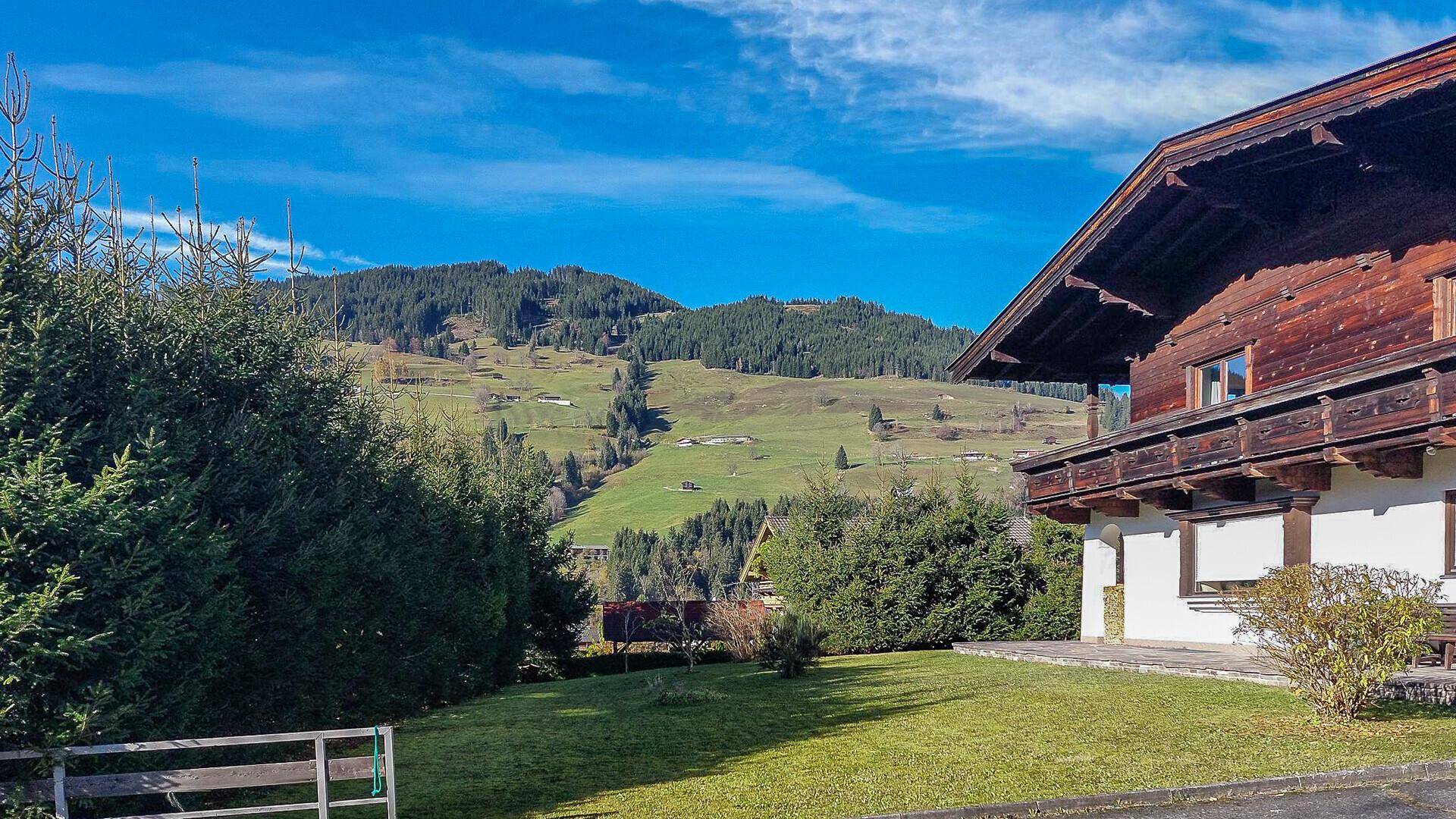 Seitenansicht eines traditionellen Hauses mit Garten und Blick auf die grünen Hügel und Berge.