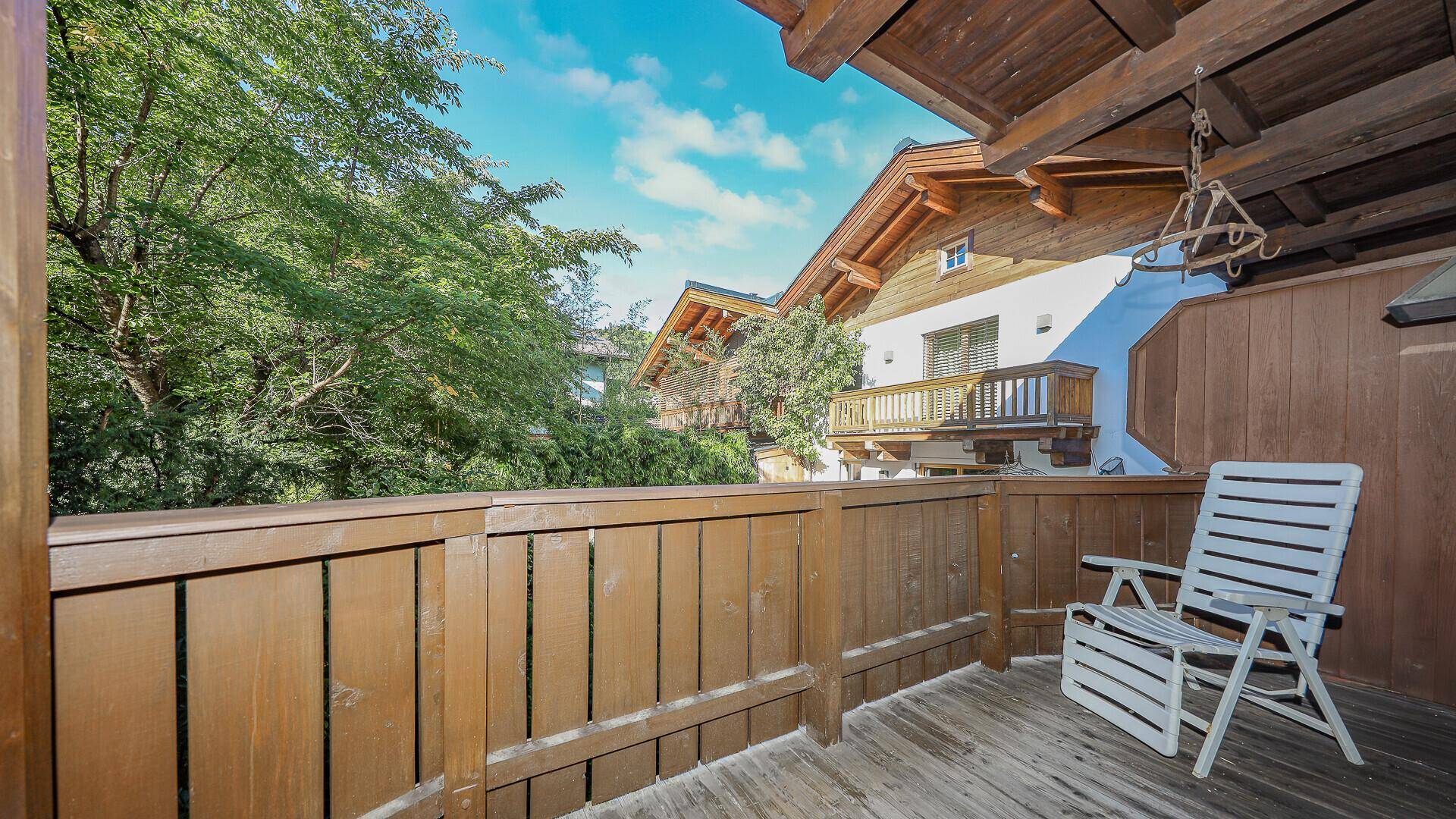 Gemütlicher Holzbalkon mit Sitzgelegenheit und Blick auf die umliegenden Häuser und Bäume.