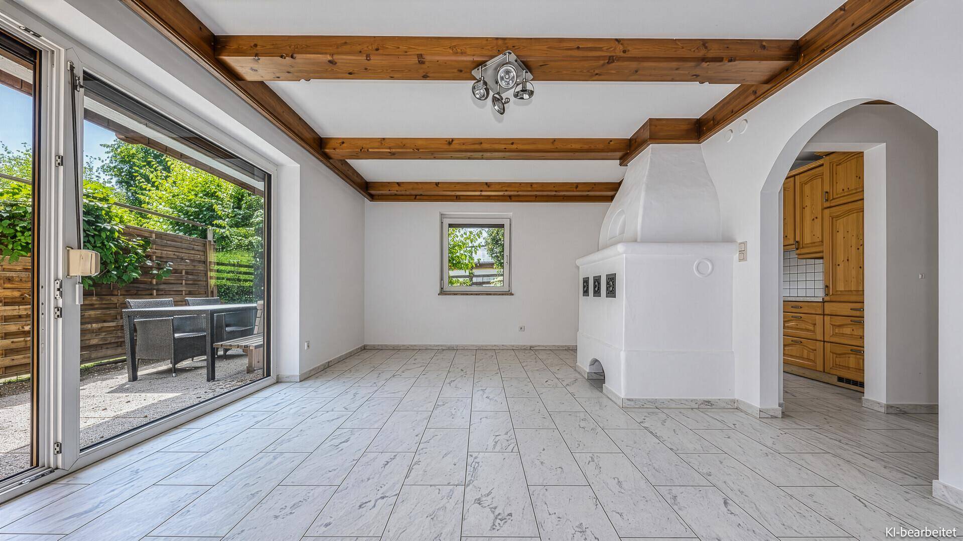 Geräumiges Wohnzimmer mit Fliesenboden, Holzbalken und traditionellem Kachelofen, mit Terrassenzugang.
