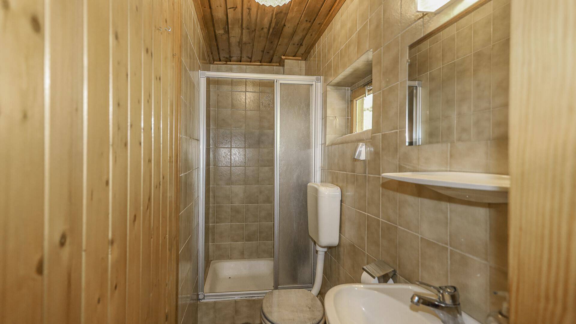Funktionales Badezimmer mit Duschkabine, WC und Waschbecken, teilweise gefliest und holzvertäfelt.
